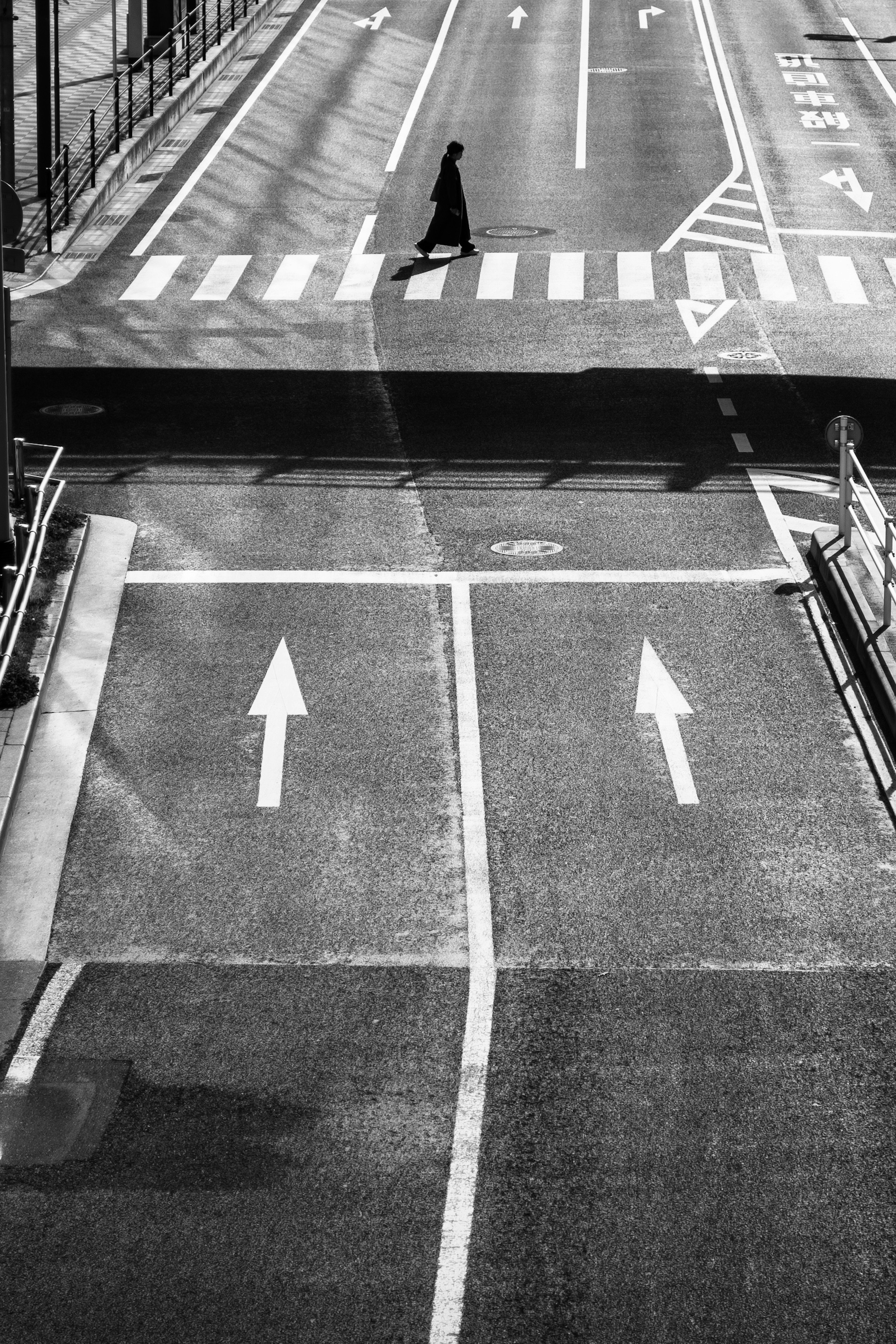 Una scena di strada in bianco e nero che mostra una persona che attraversa il marciapiede e frecce a un incrocio