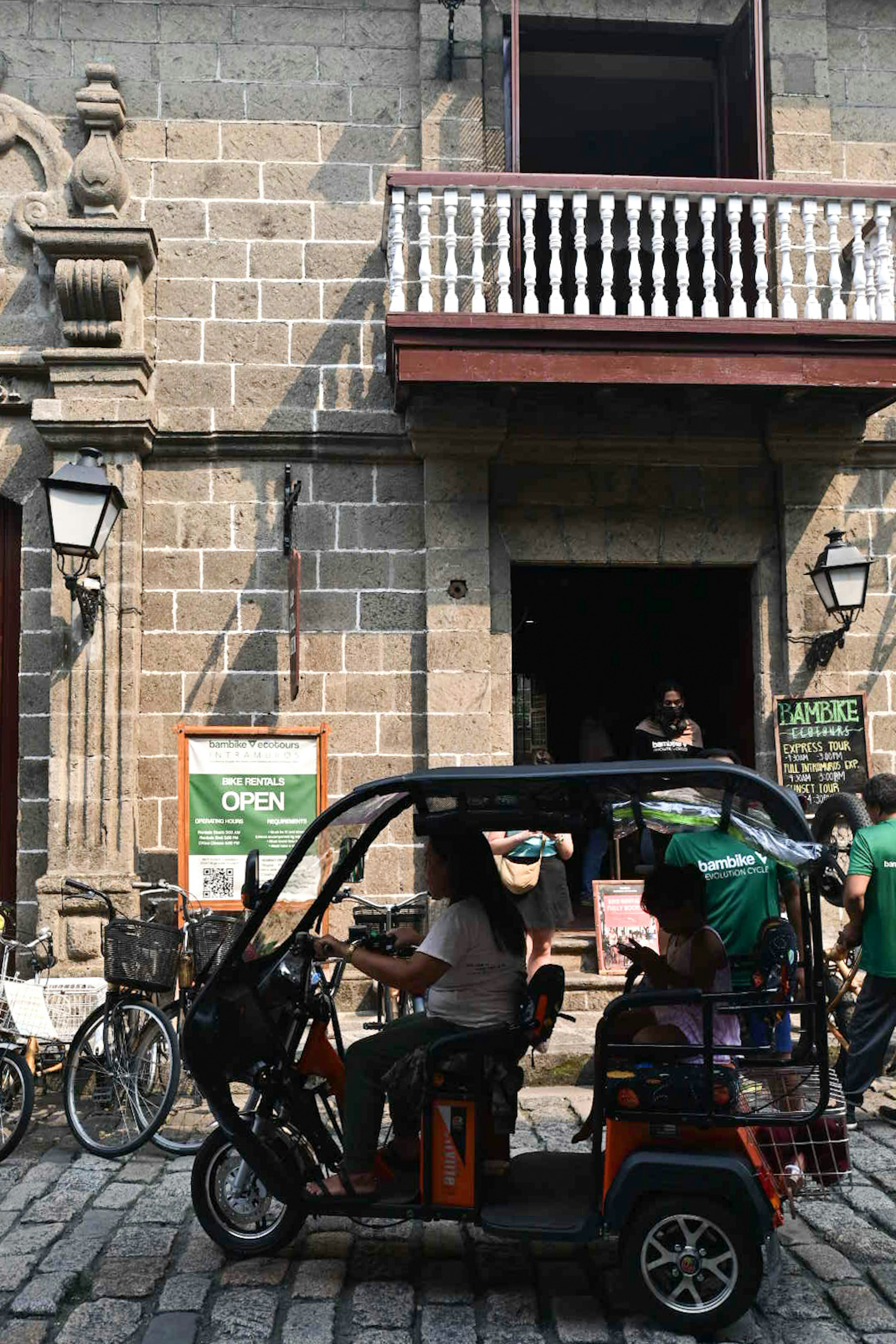 Tricycle passing in front of a historic stone building with a balcony