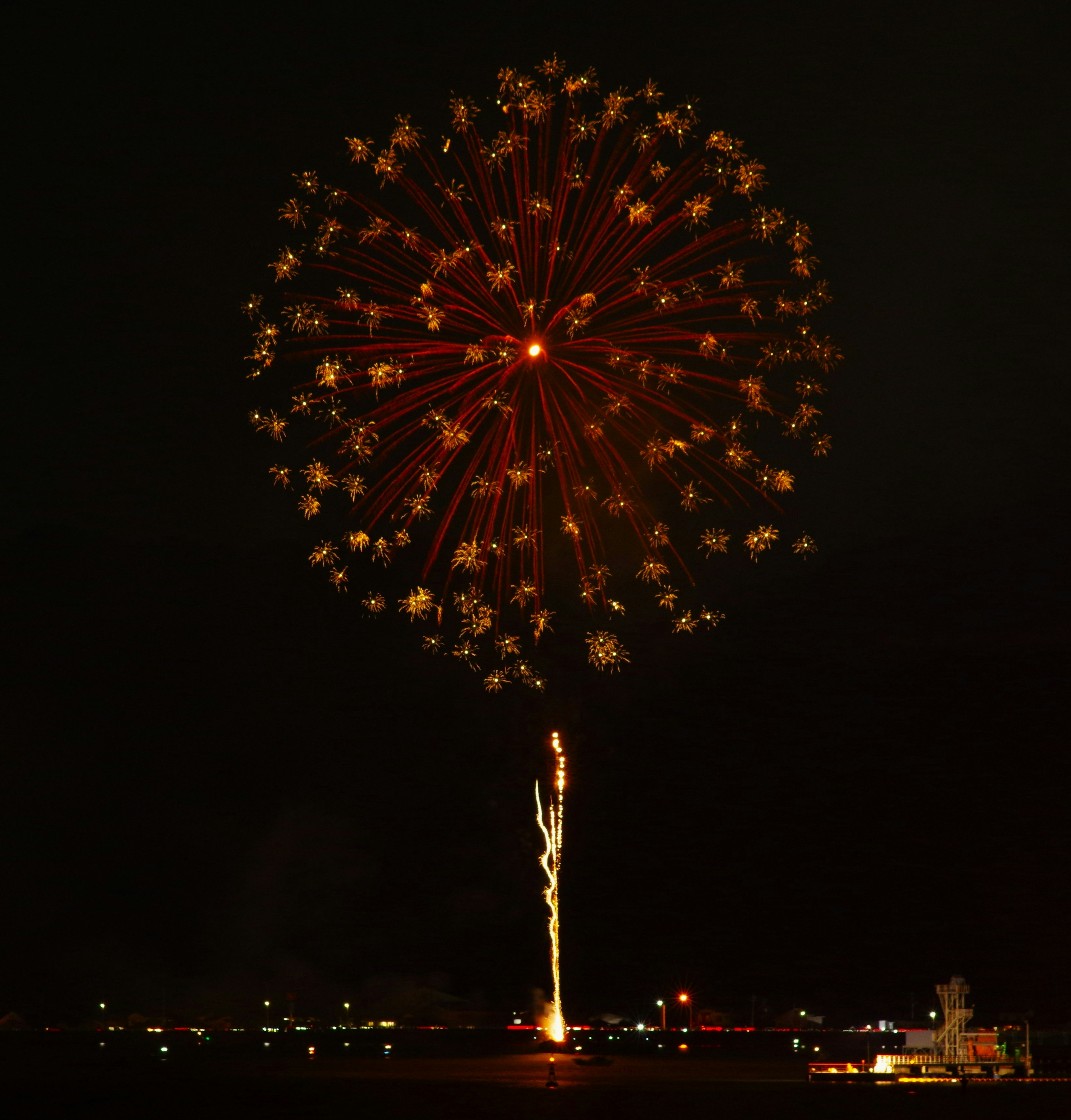 Large firework display bursting in the night sky featuring red and gold colors