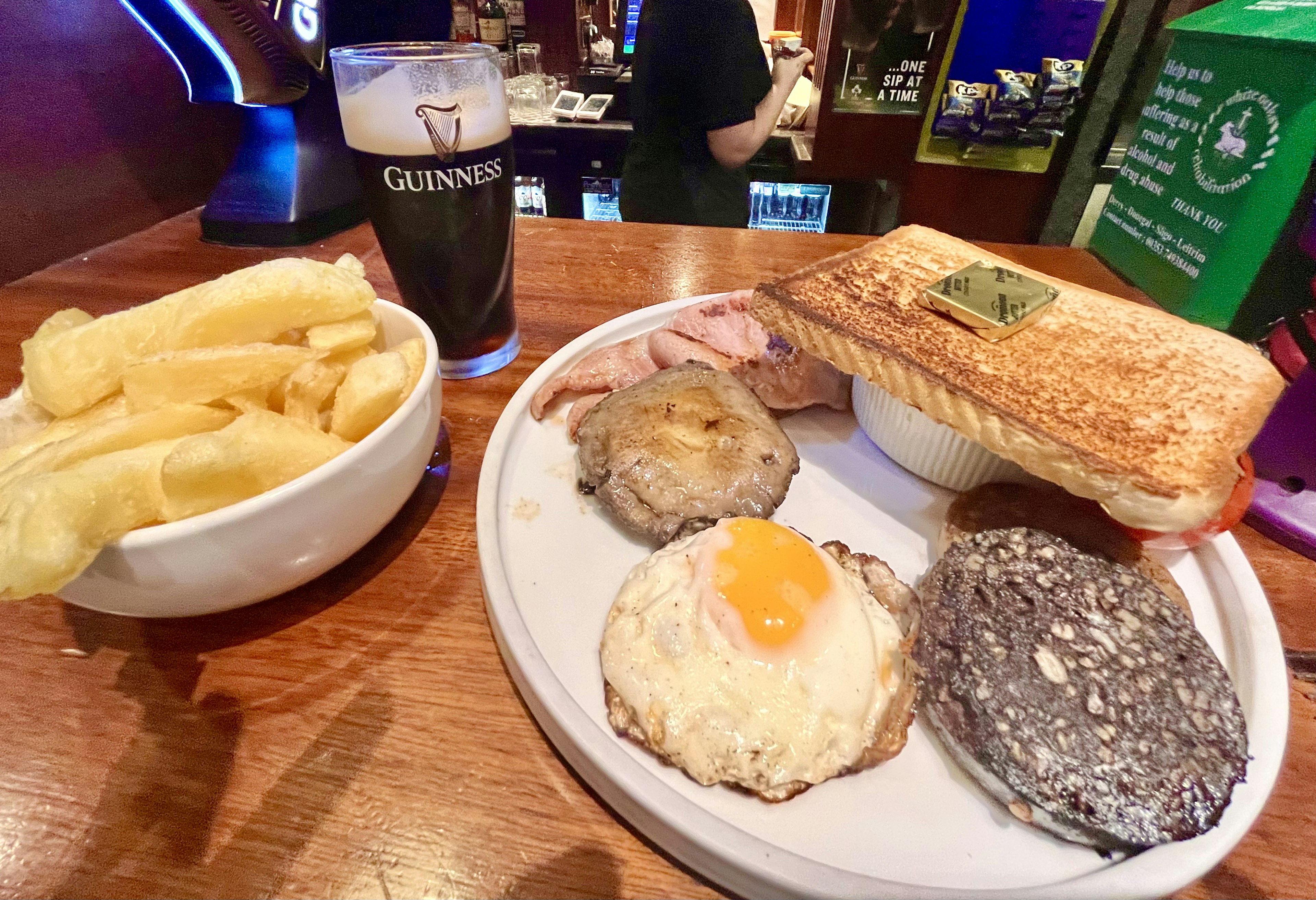 グラスに入ったギネスビールとプレートに載った朝食料理 サンドイッチ、目玉焼き、ソーセージ、ブラックプudding、フライドポテト