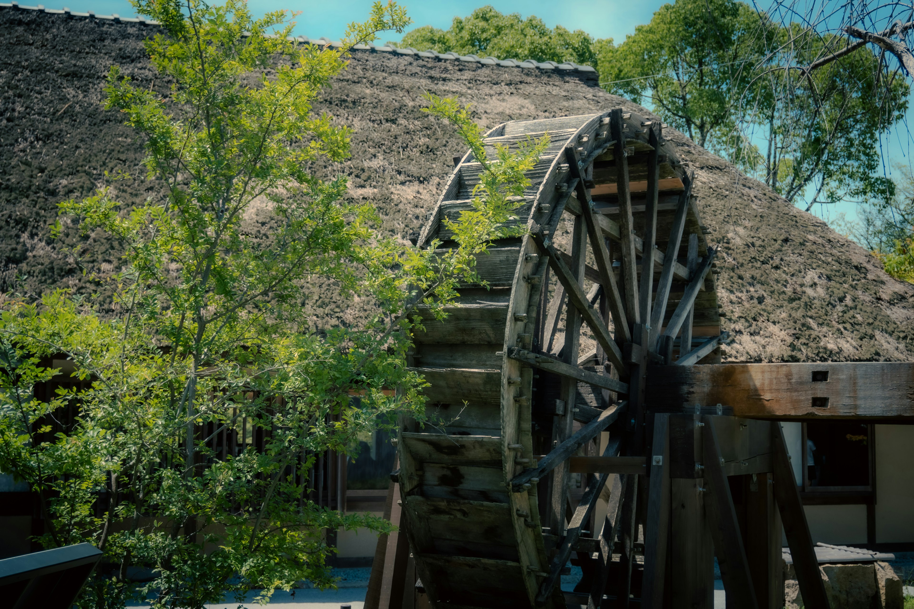 Une roue à eau traditionnelle à côté d'un bâtiment au toit de chaume entouré de verdure