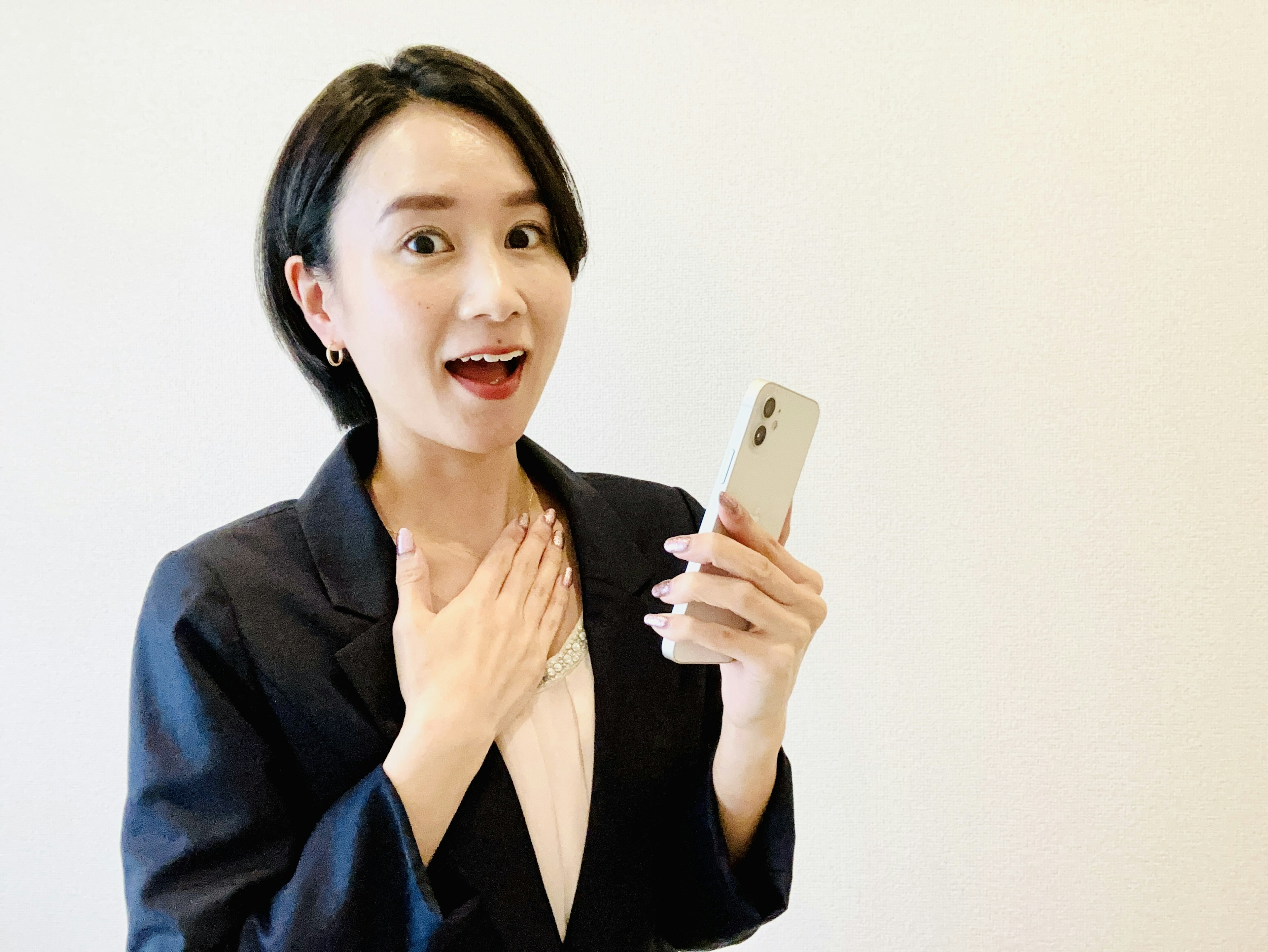 A woman in business attire holding a smartphone with a surprised expression