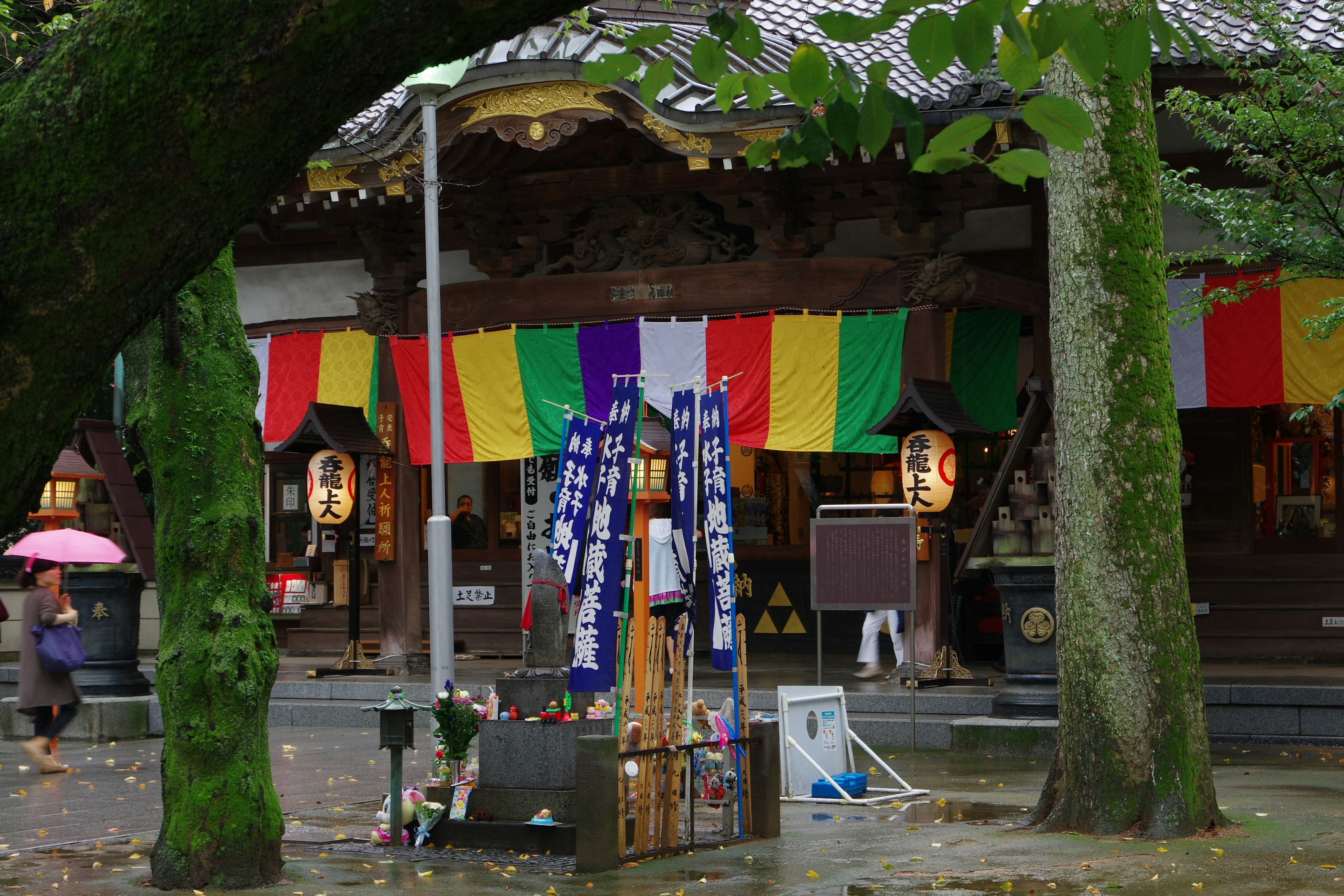 Colorful banners at the entrance of a shrine with festival decorations and trees