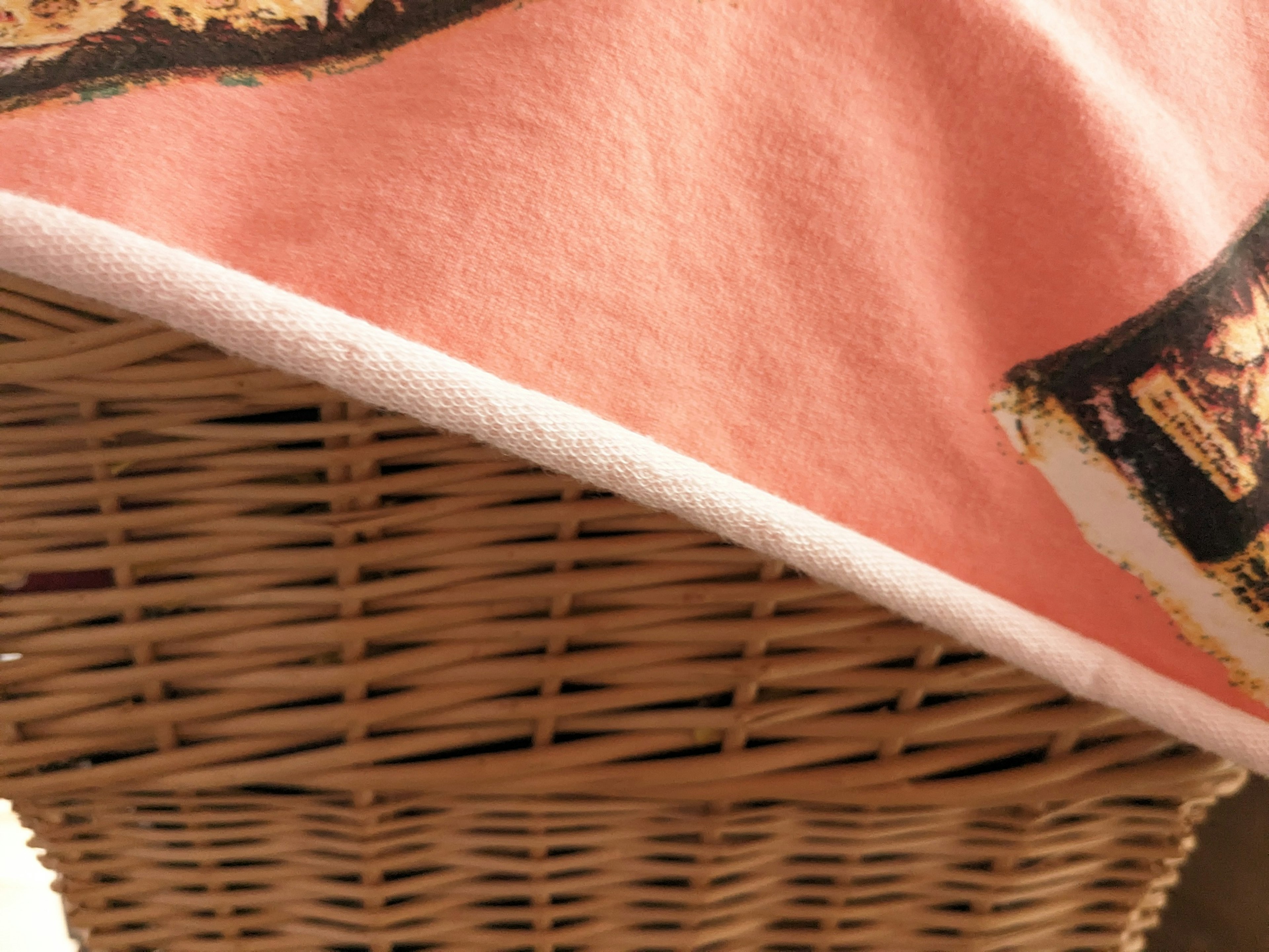 A portion of a pink blanket draped over a woven basket