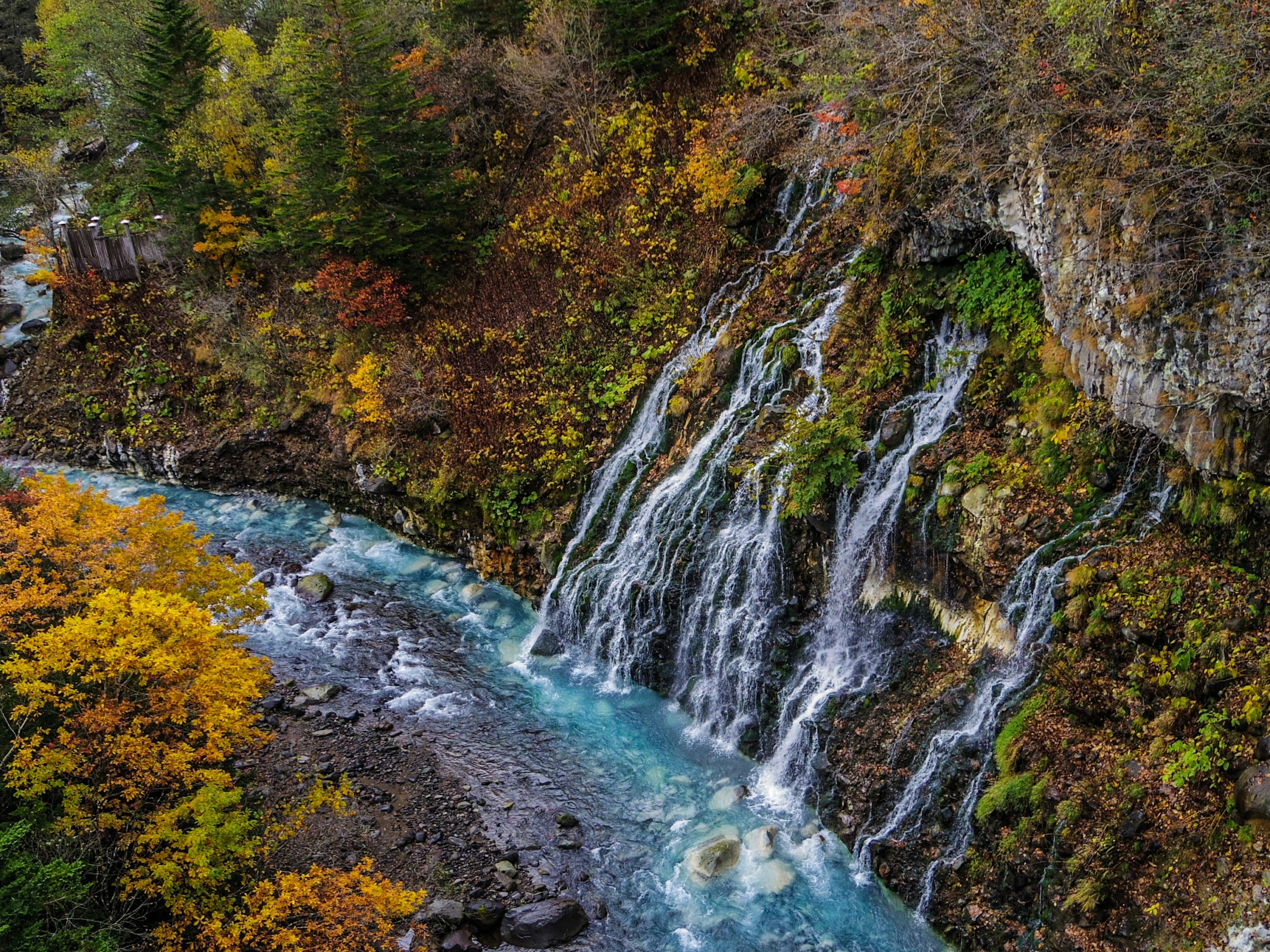 Hermosa cascada que cae en un río azul rodeado de follaje otoñal