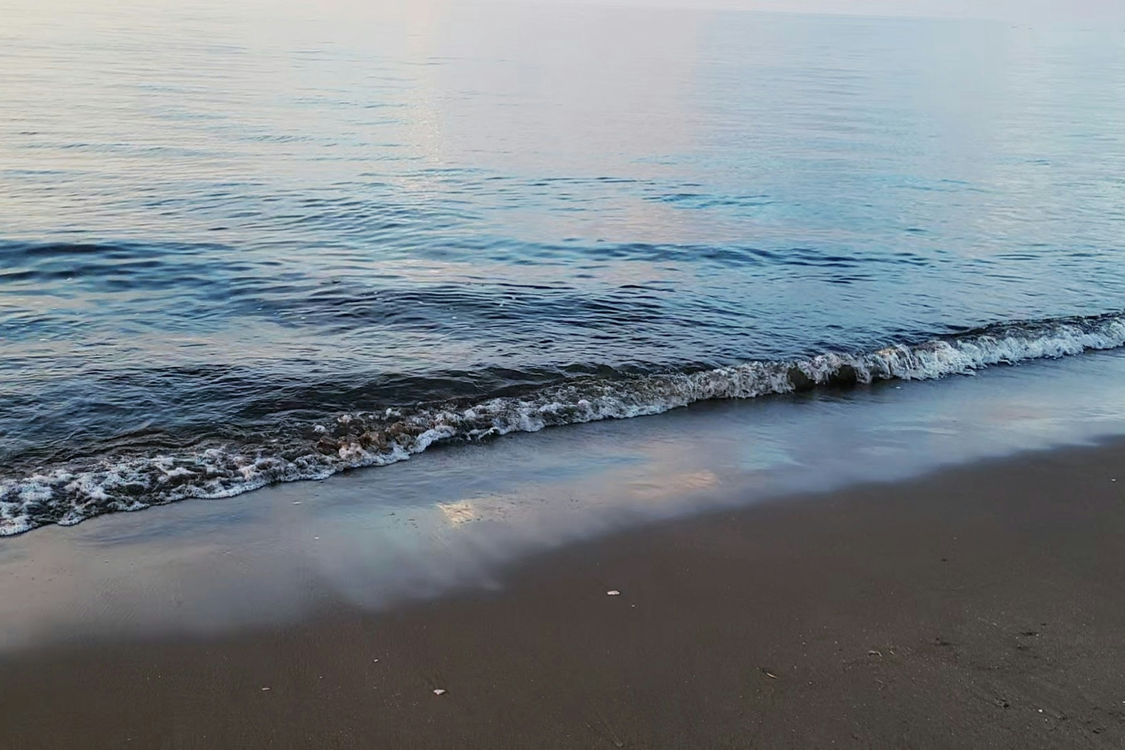 Pemandangan laut tenang dan pantai berpasir pantulan matahari terbenam di permukaan air