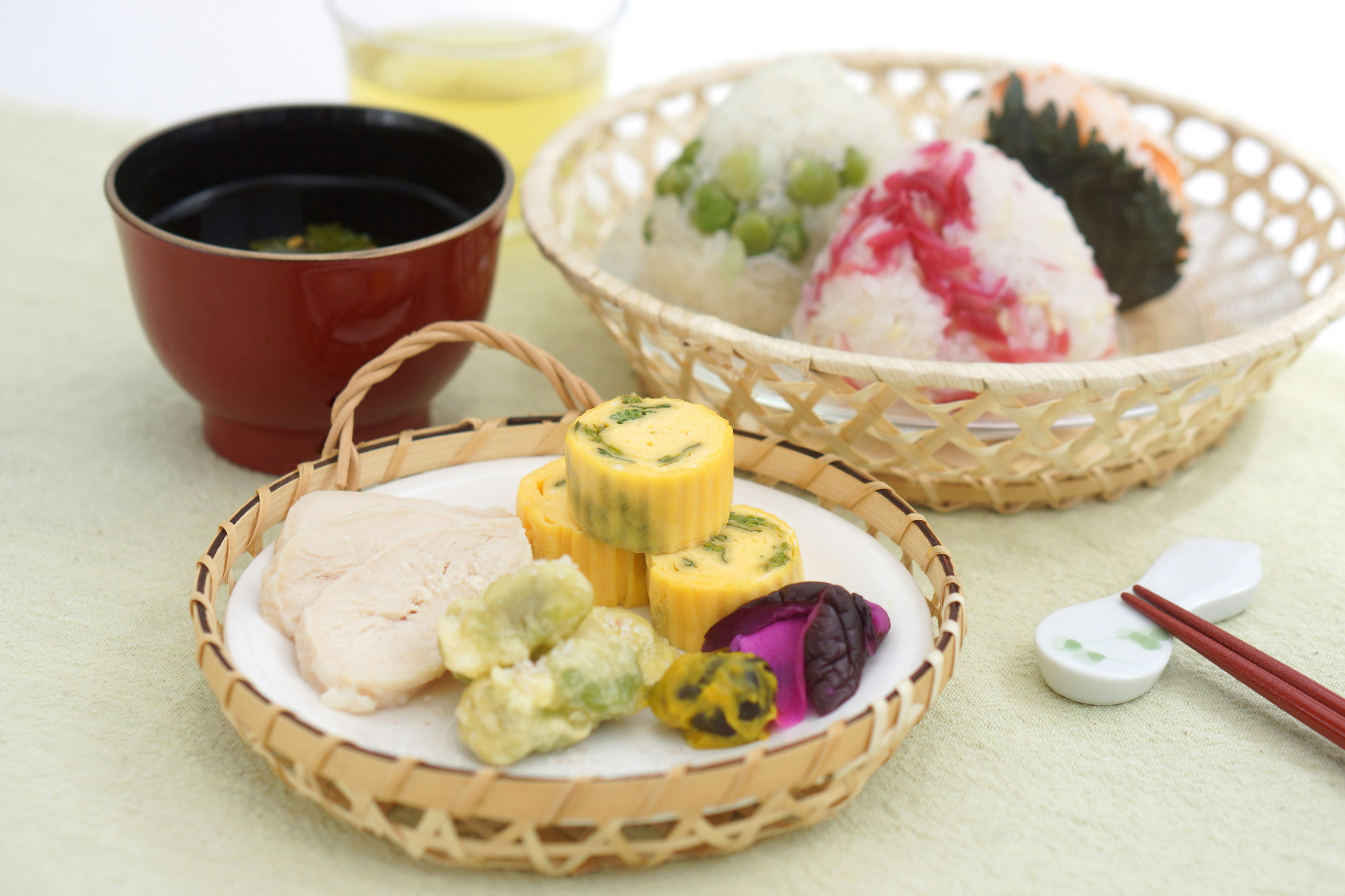 Traditional Japanese food arrangement featuring colorful onigiri rice balls, tamagoyaki, pickles, and green tea