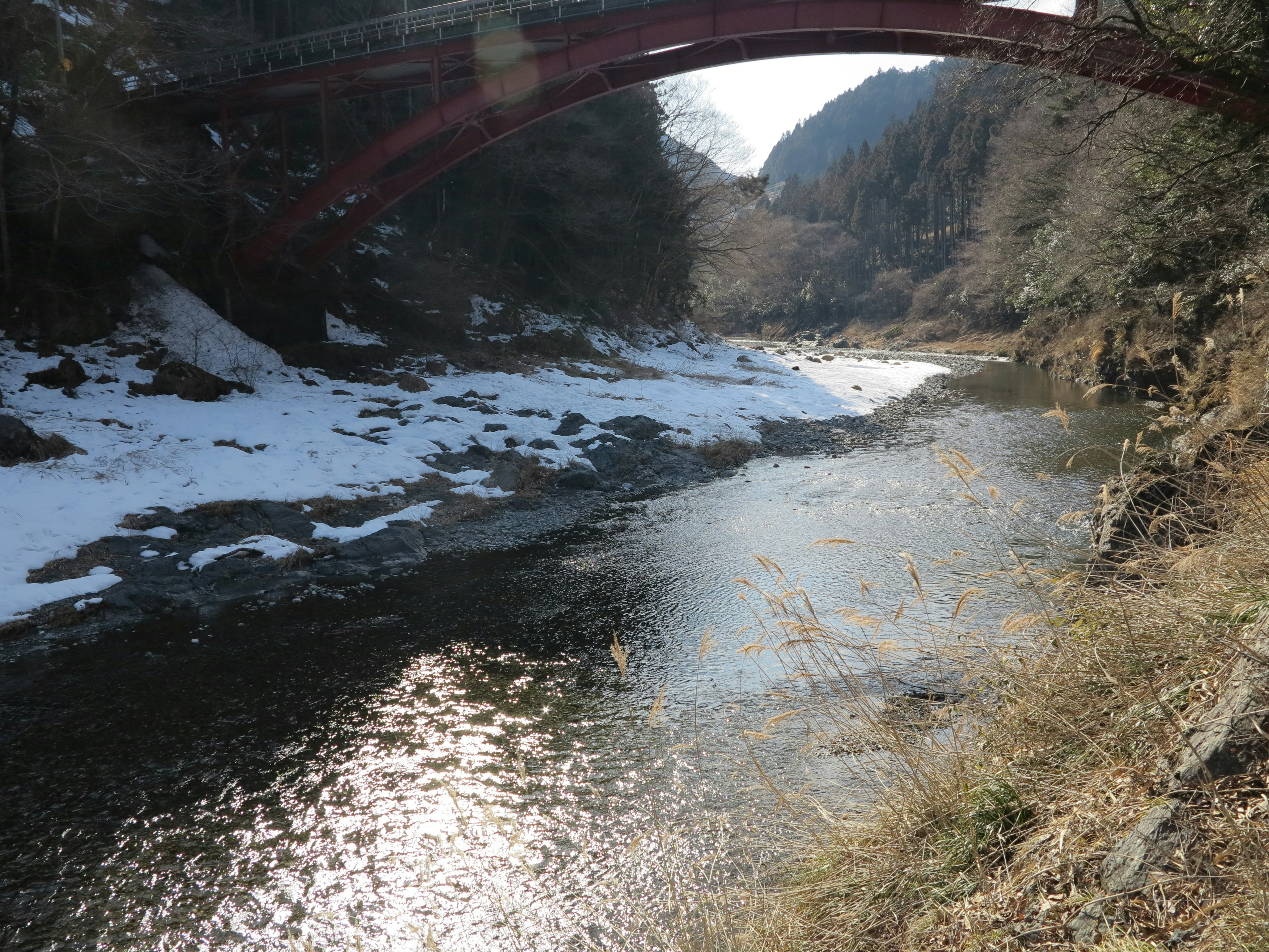 Vue pittoresque d'une rivière avec un pont rouge et des rives couvertes de neige