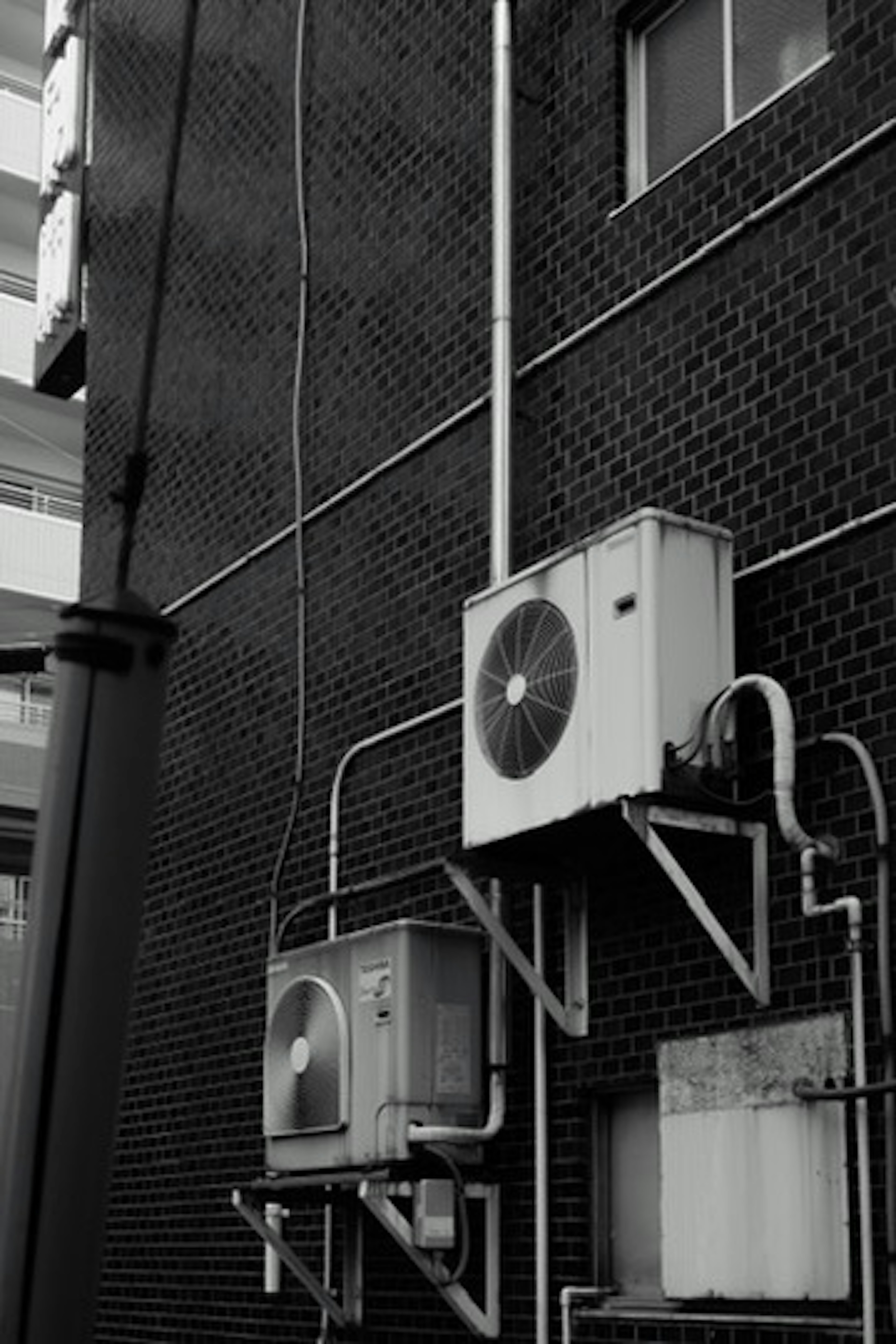 Deux unités de climatisation montées sur un mur en briques noires avec des tuyaux visibles