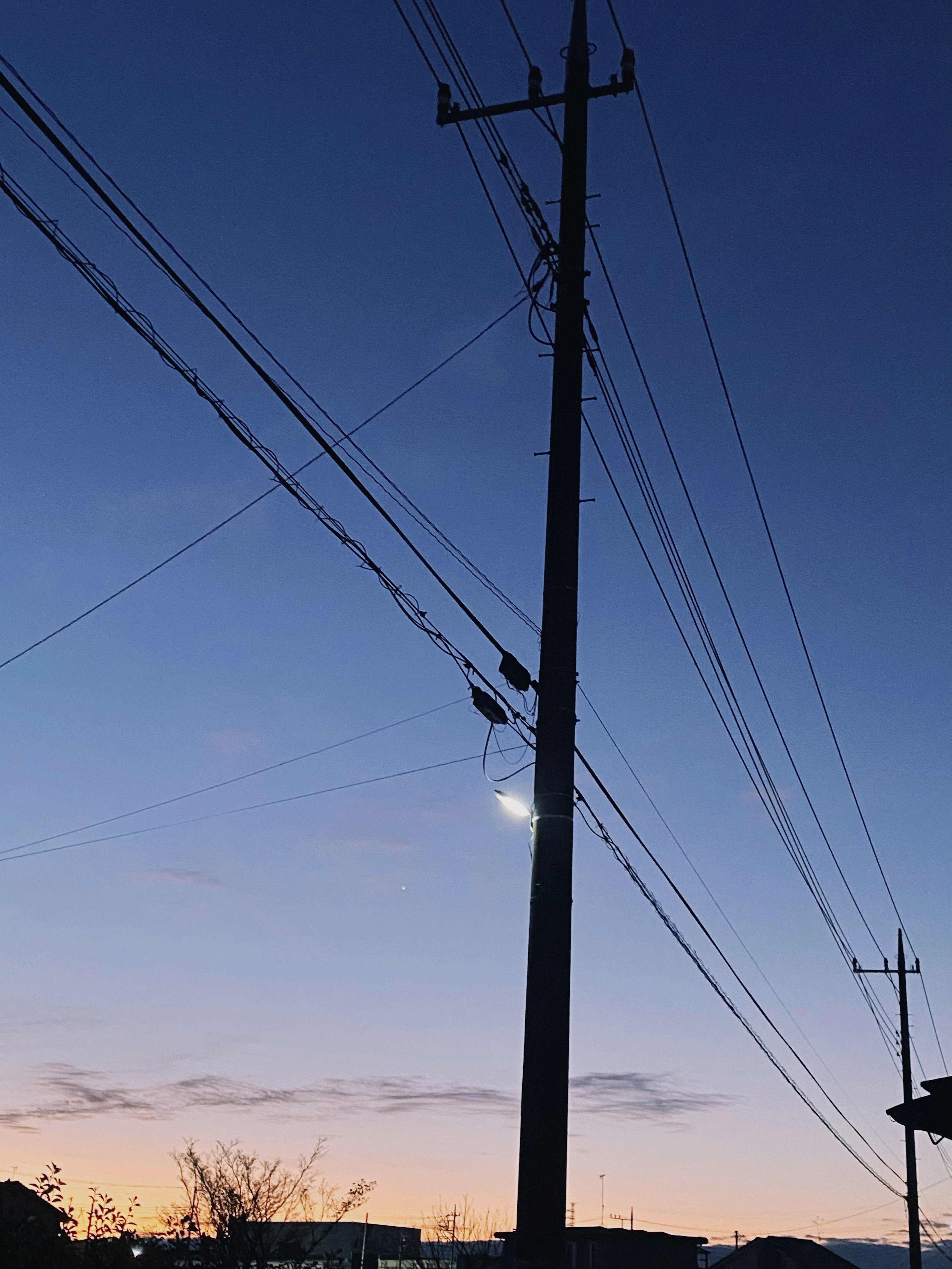 Silueta de un poste de luz y líneas eléctricas contra un cielo crepuscular