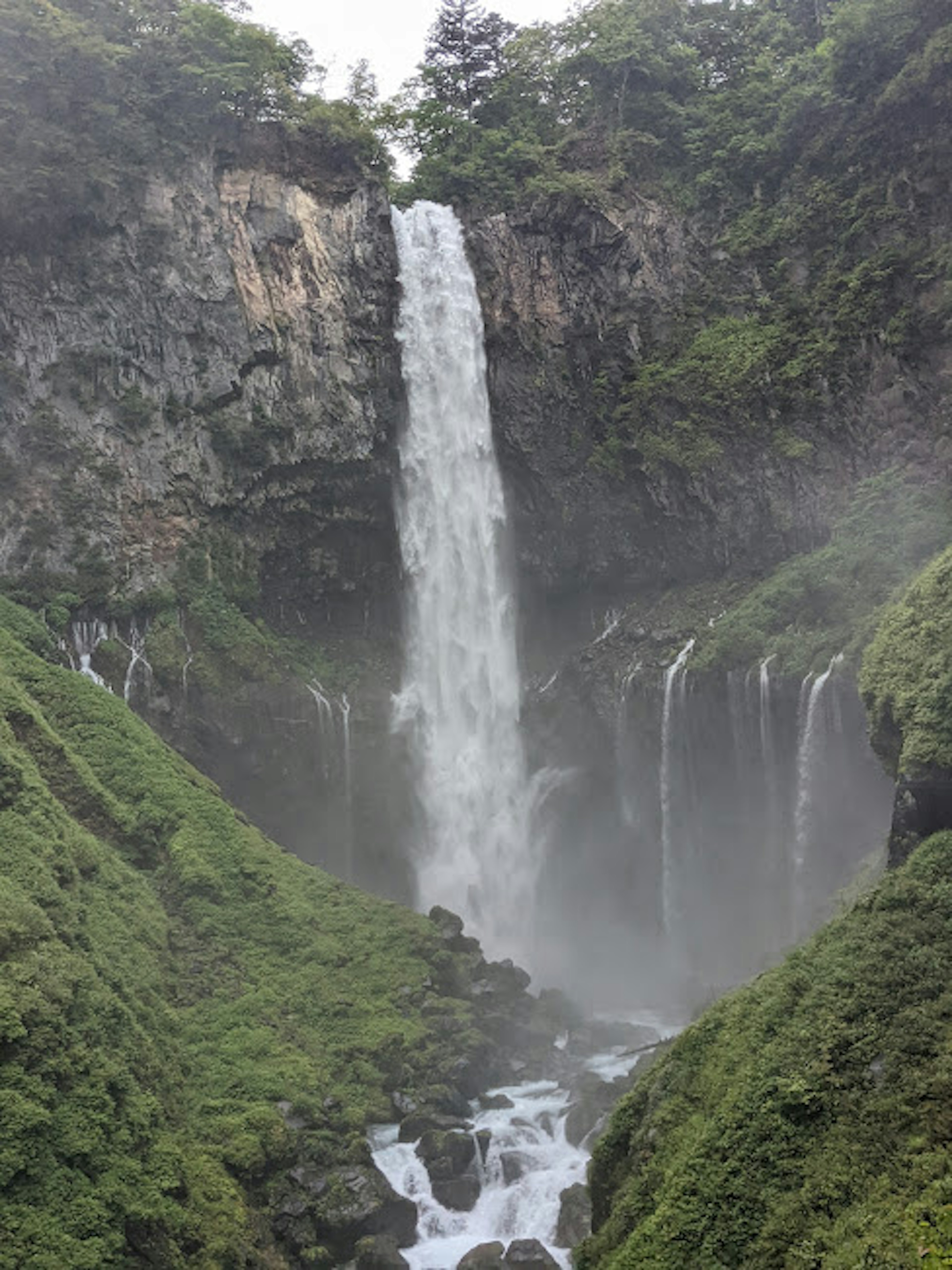 Cascata maestosa circondata da montagne verdi e nebbia