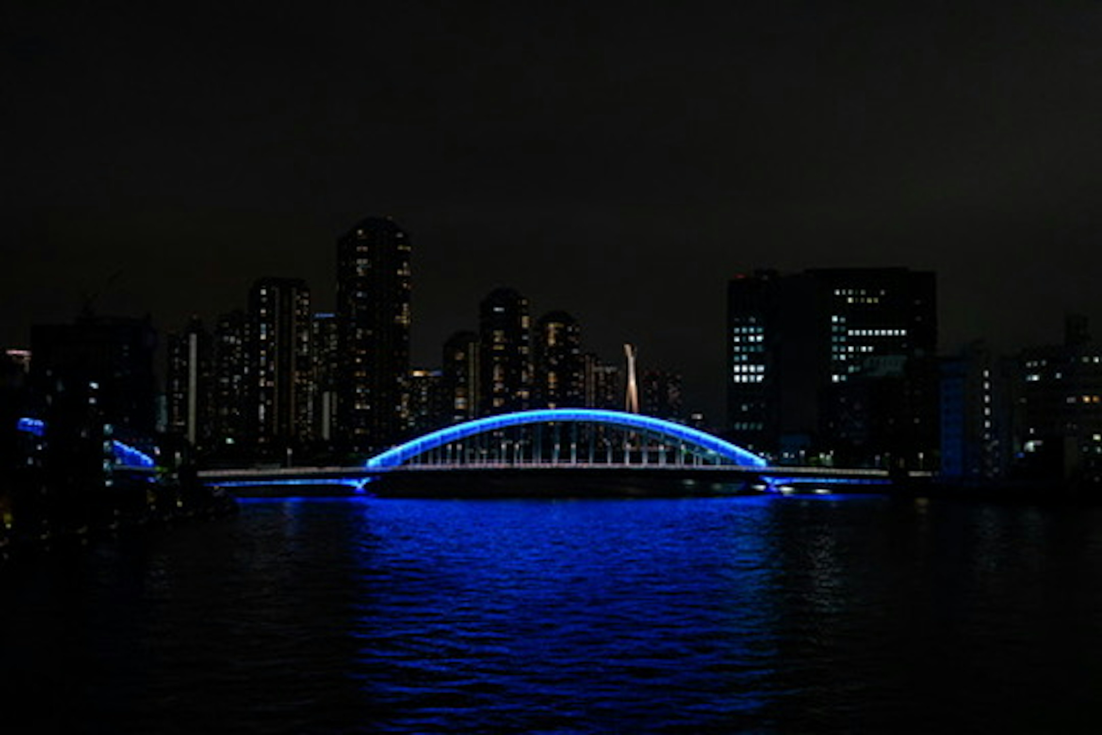 Beleuchtete blaue Bogenbrücke vor einer Stadtsilhouette bei Nacht