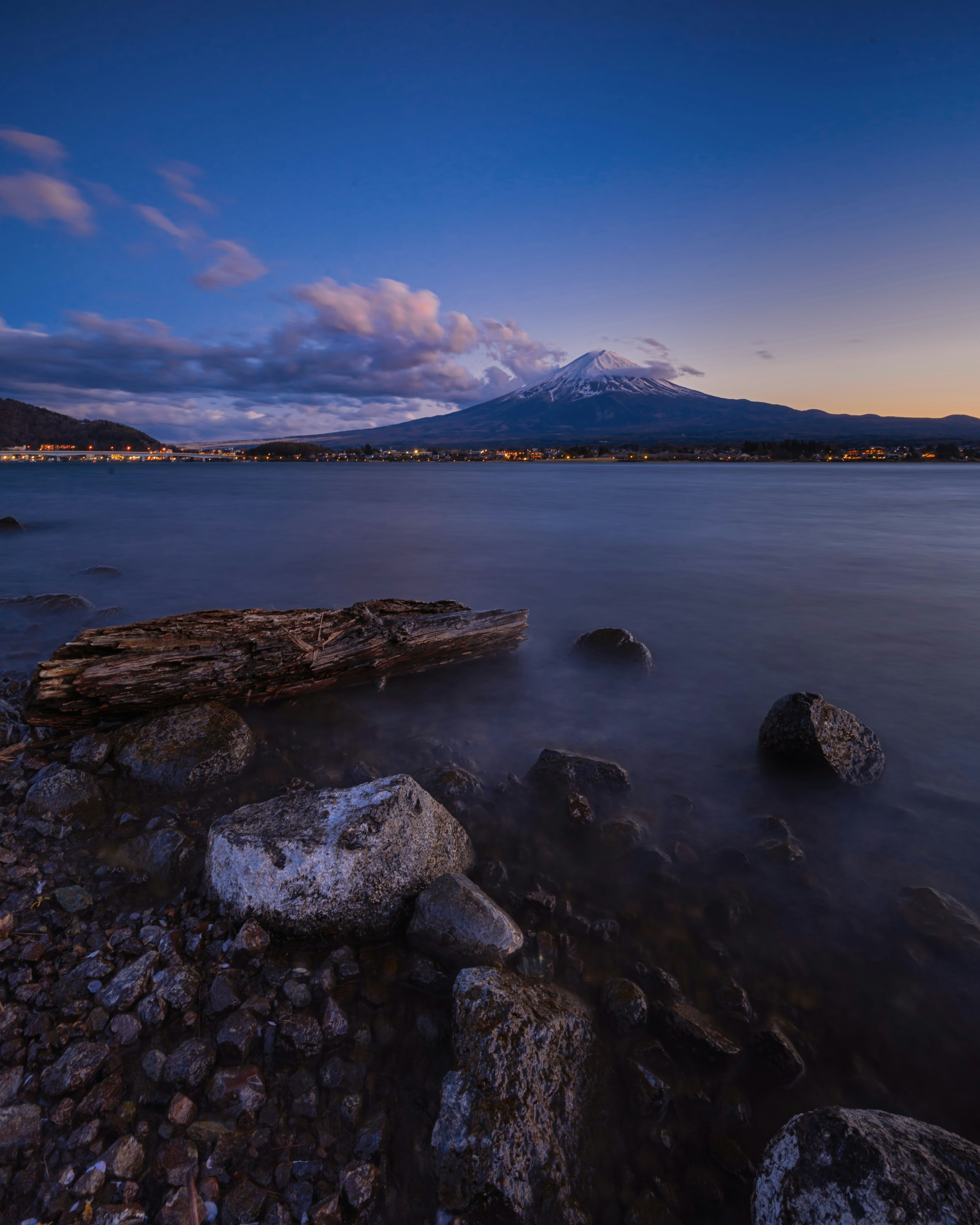 青い空と雲が広がる湖畔の風景 山が背景にあり 岩と木の残骸が手前に見える