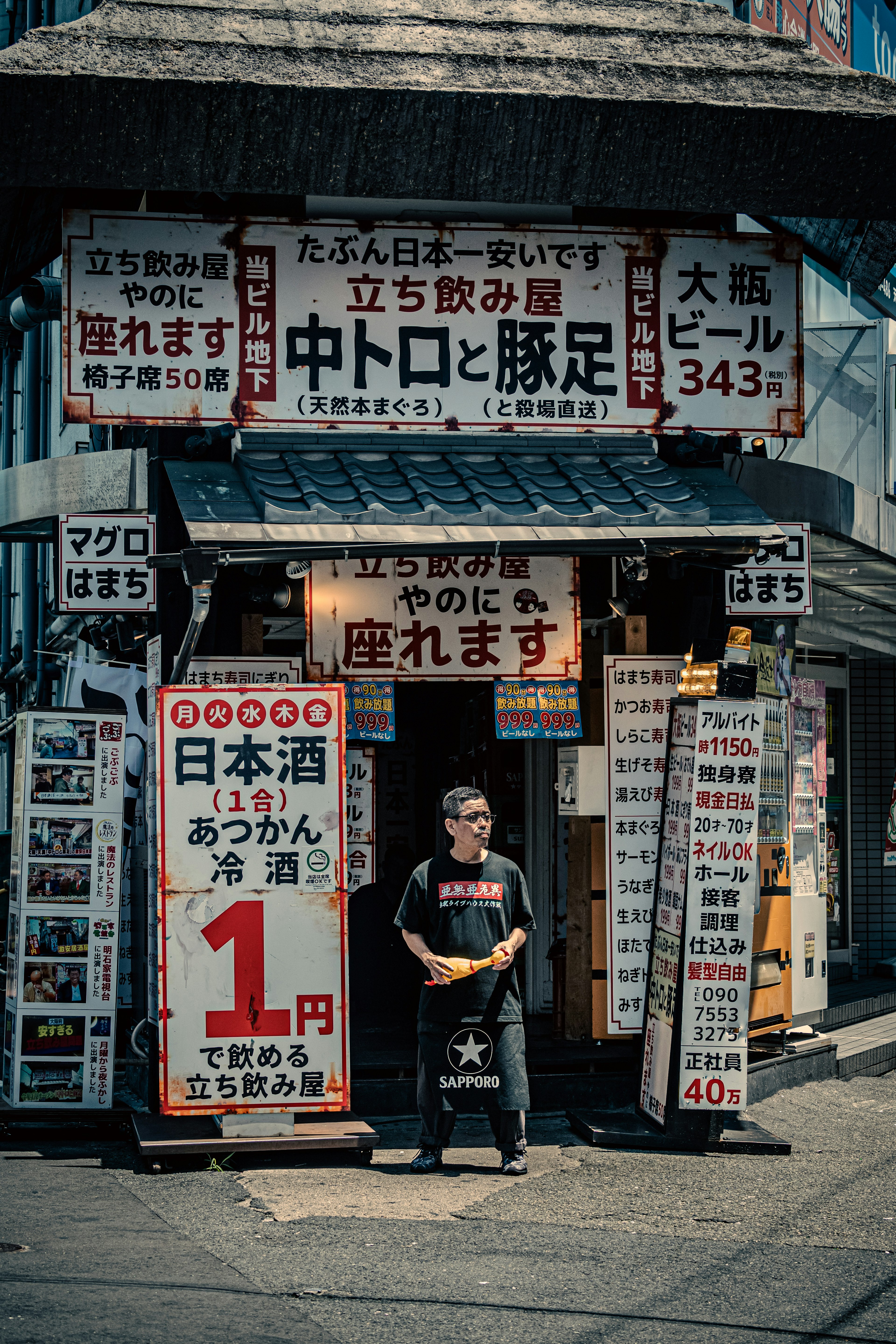 A man standing in front of a busy Japanese eatery with signs displaying menu items and prices in Japanese