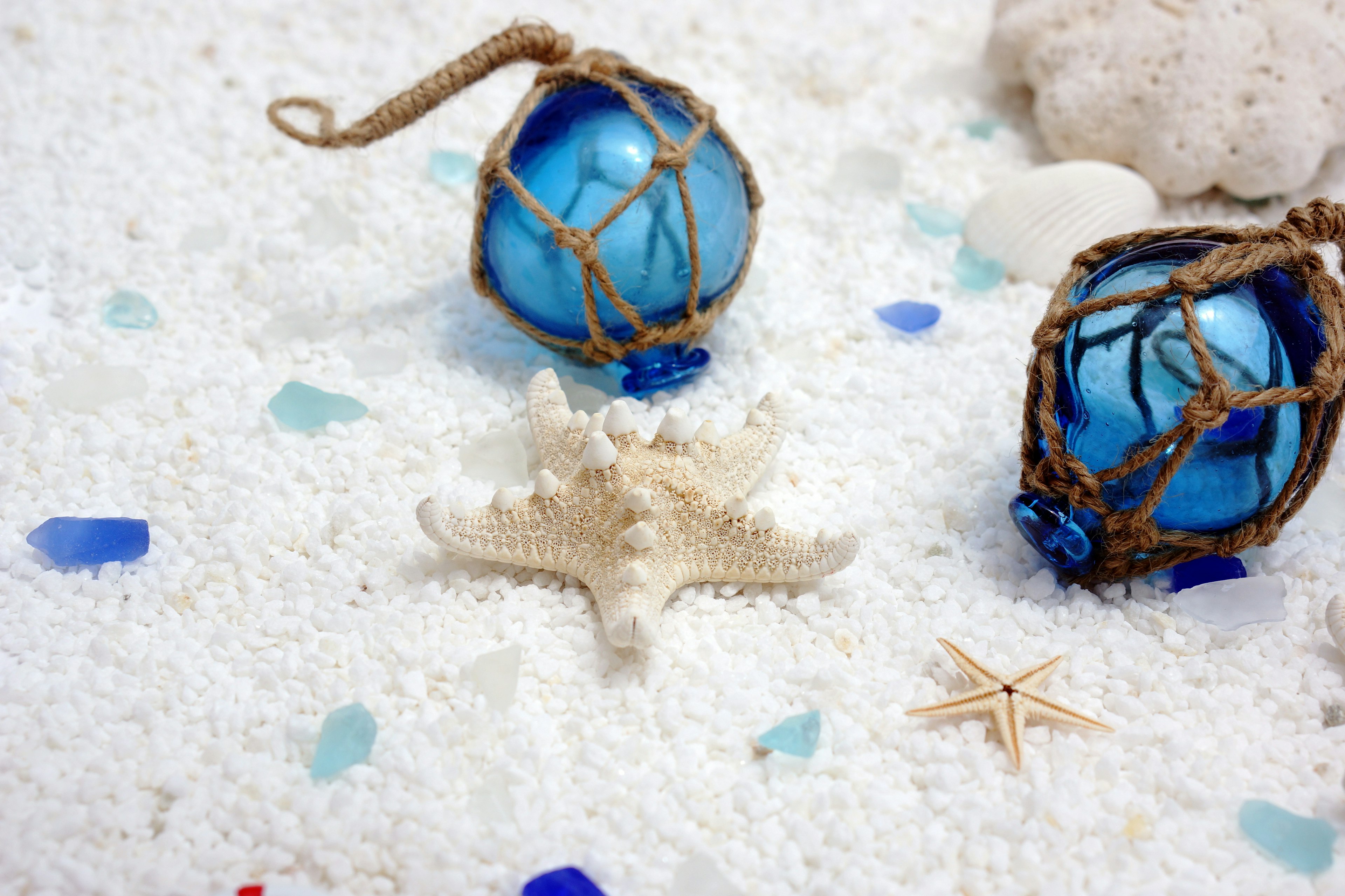 Decoración de playa con bolas de vidrio azul y estrellas de mar dispuestas sobre arena blanca