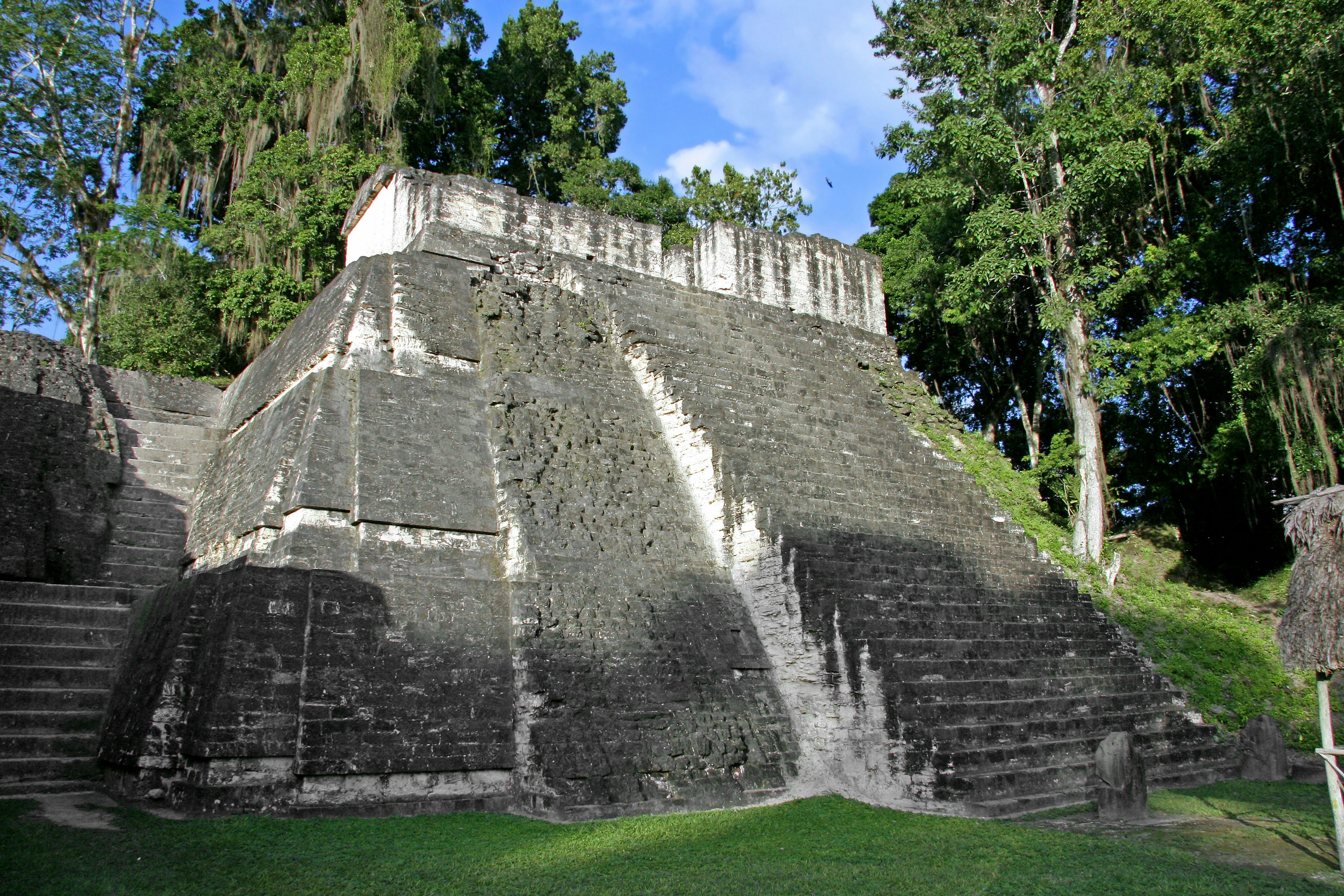 Seitenansicht einer alten Stufenpyramide umgeben von Grün und blauem Himmel