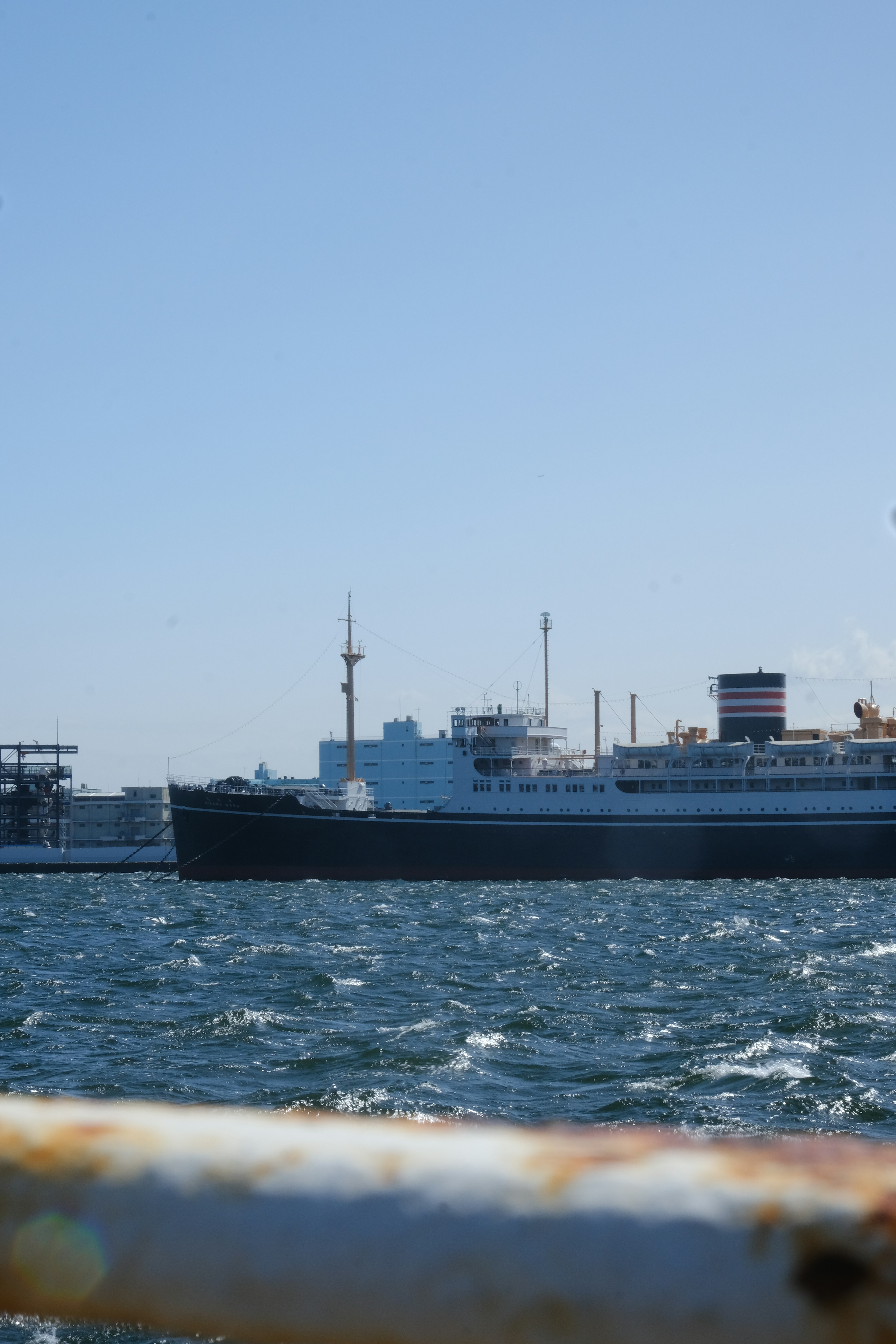 An old passenger ship sailing on the sea with a harbor in the background