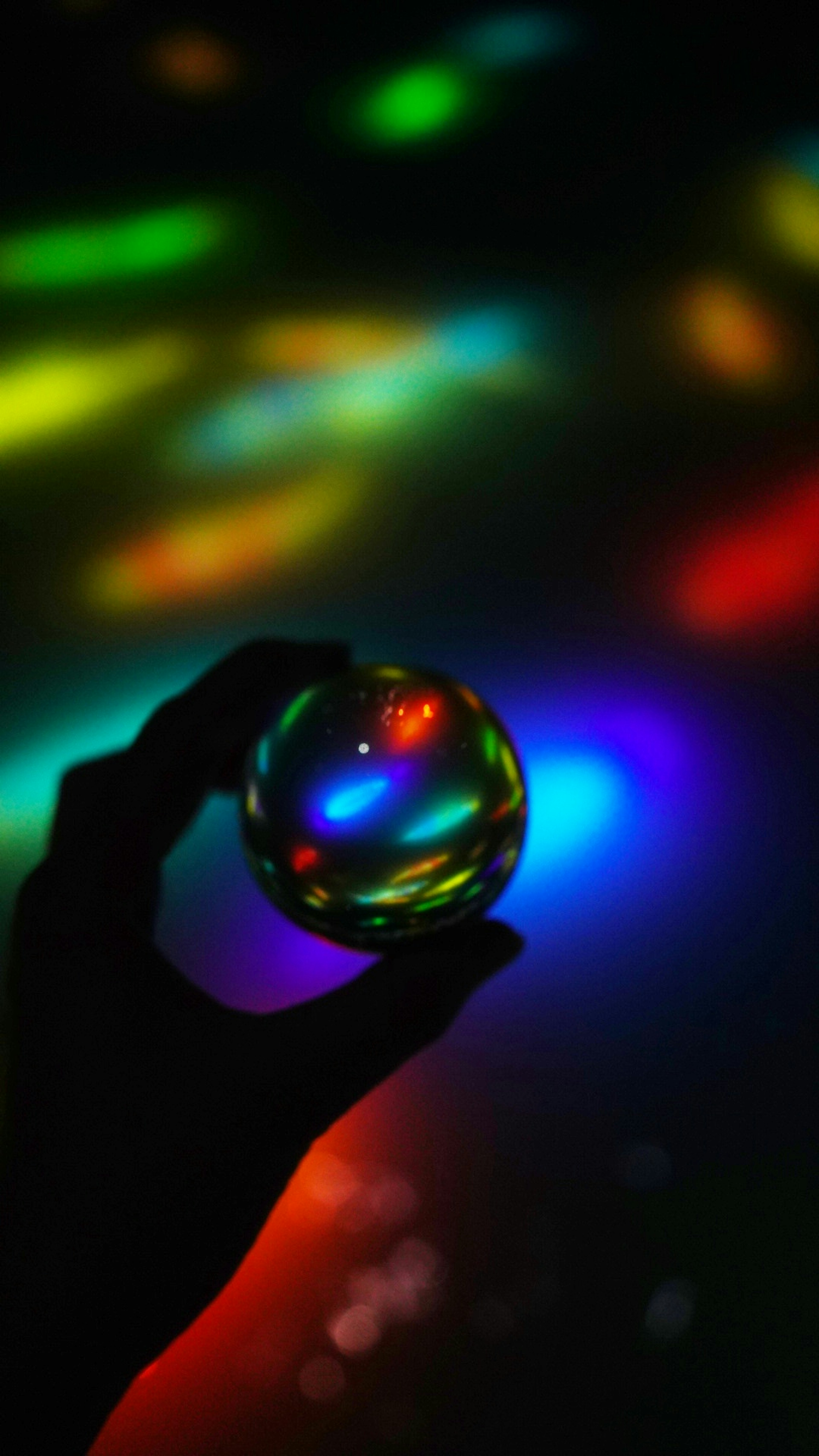 Imagen de una bola de cristal que refleja luces coloridas sostenida en una mano