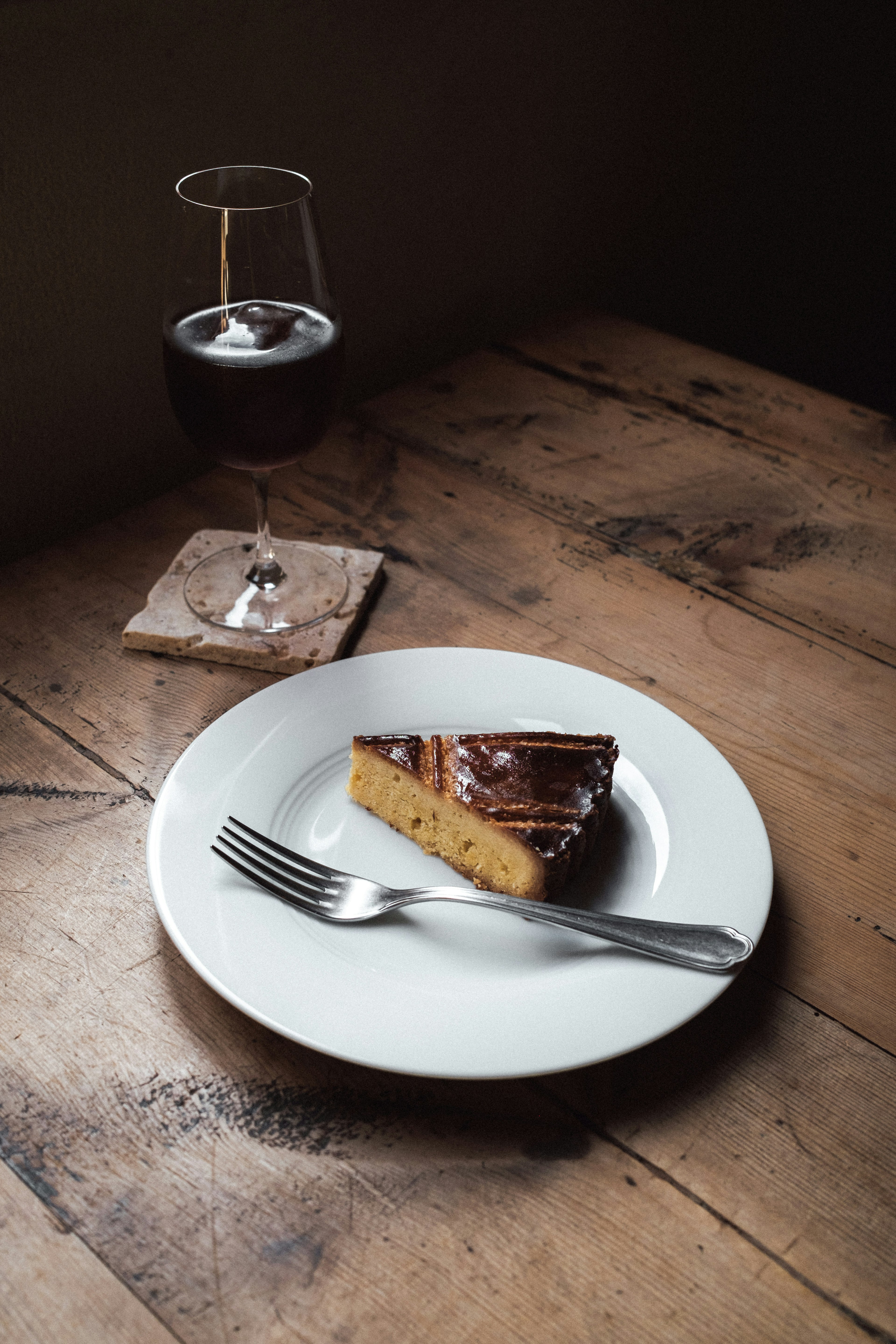 Una porción de pastel en un plato blanco con una copa de vino tinto