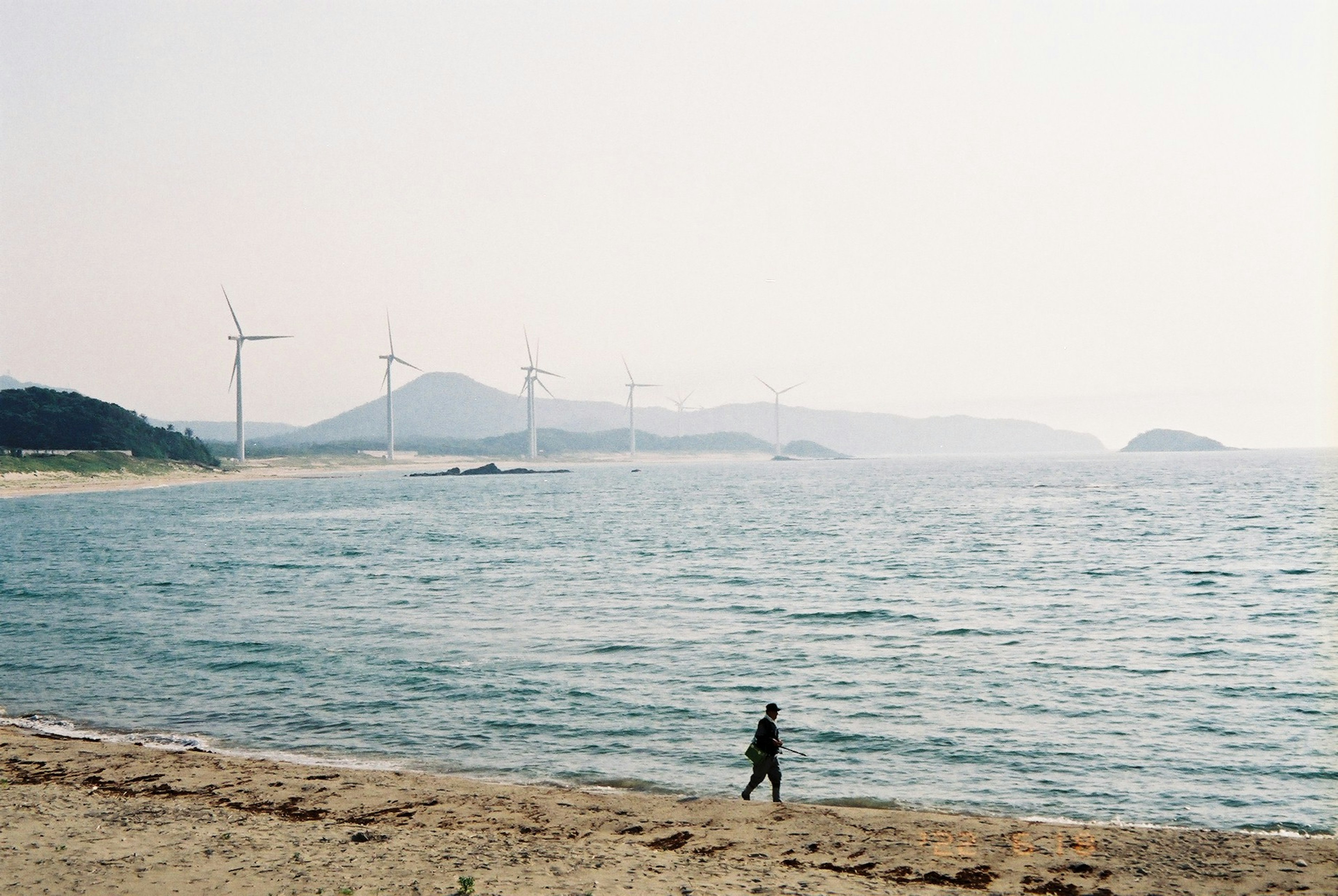 海岸を歩く人と風力発電機が並ぶ風景