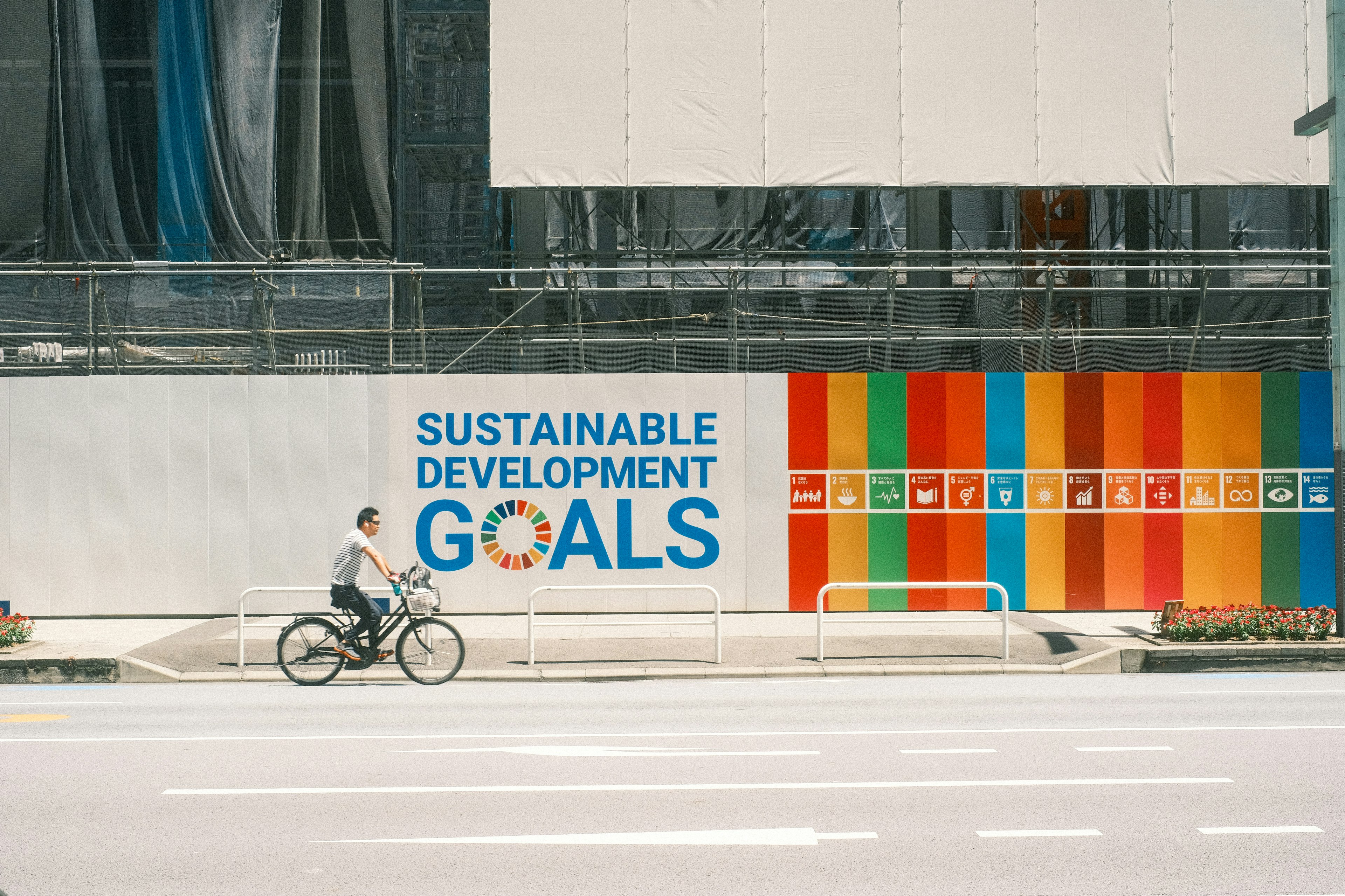 Person riding a bicycle past a mural of Sustainable Development Goals