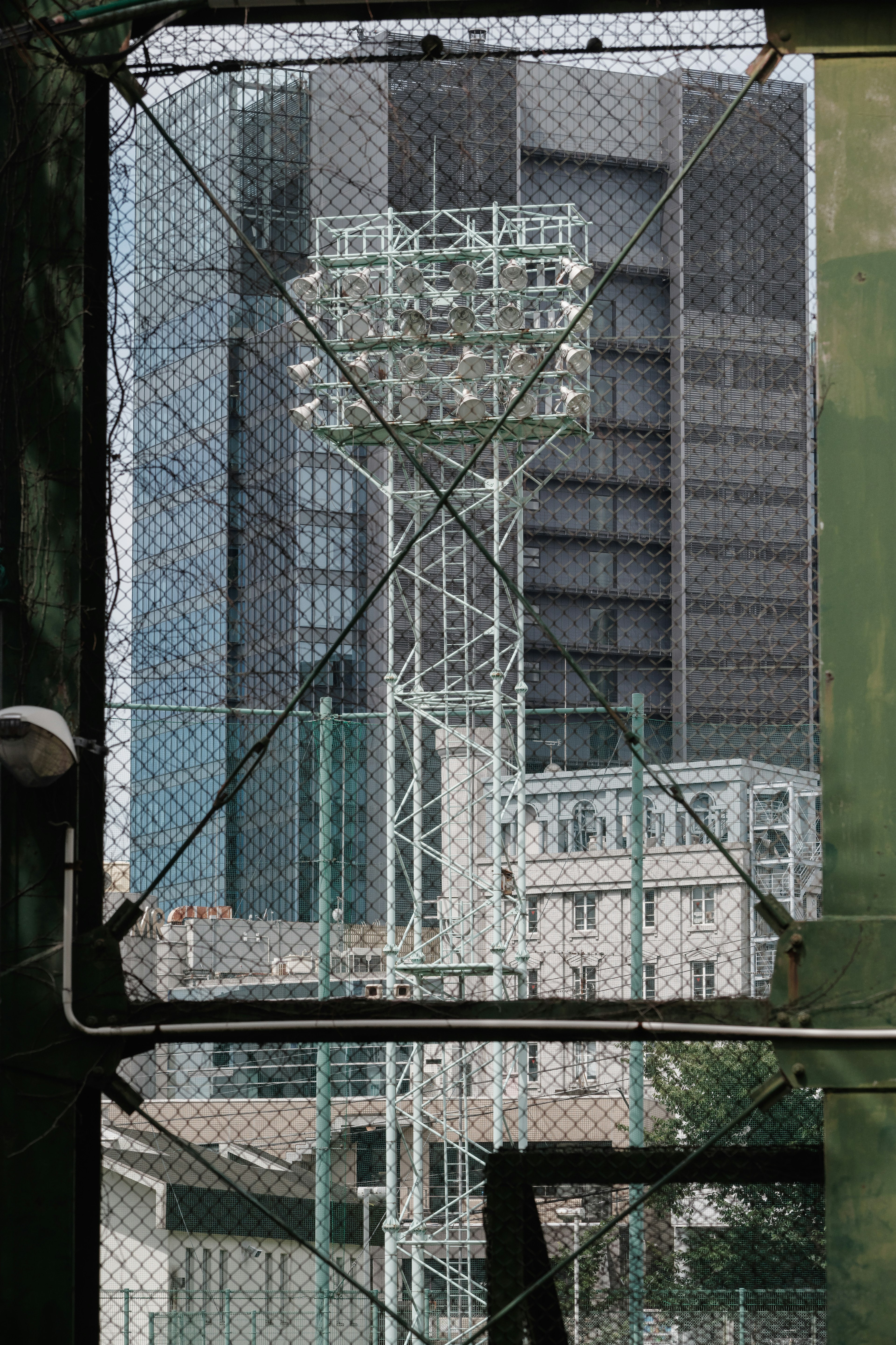 Tall building and floodlight tower seen through a fence