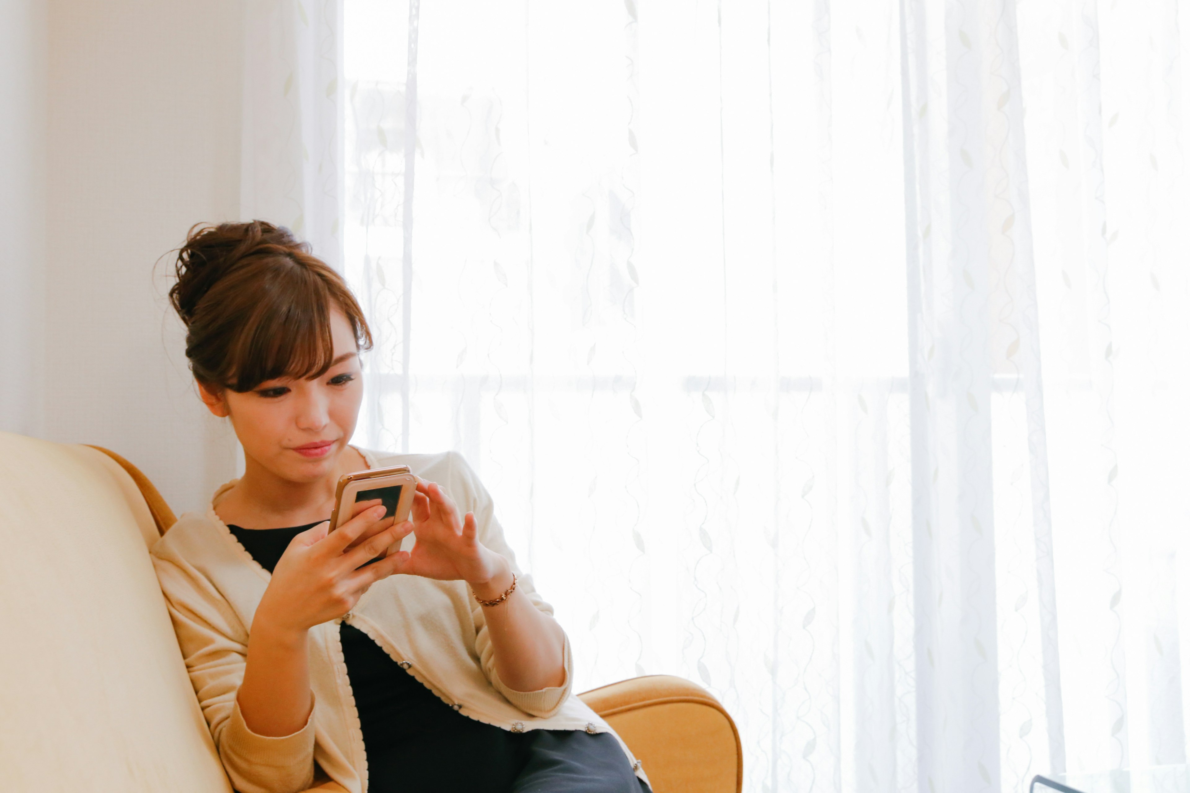 Seorang wanita duduk di sofa melihat smartphone-nya