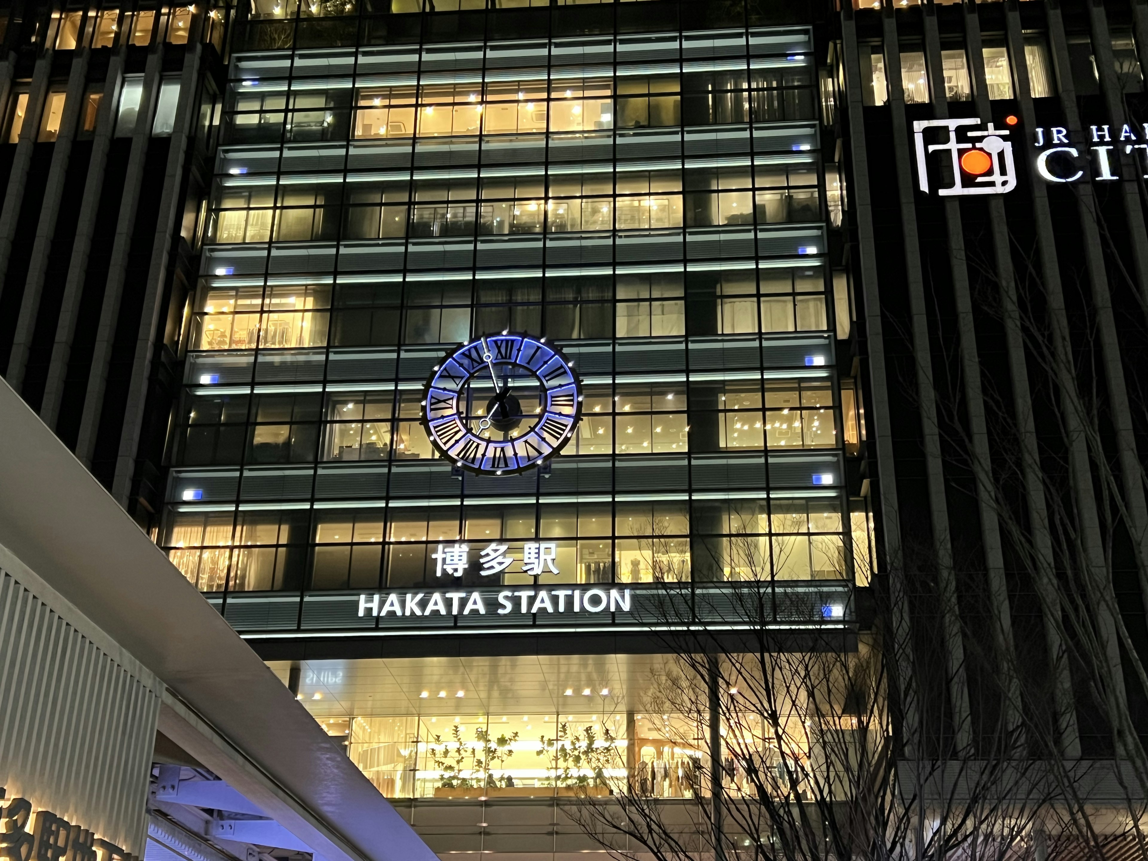 Vista nocturna de la estación de Hakata con luces brillantes y arquitectura moderna con un diseño de reloj