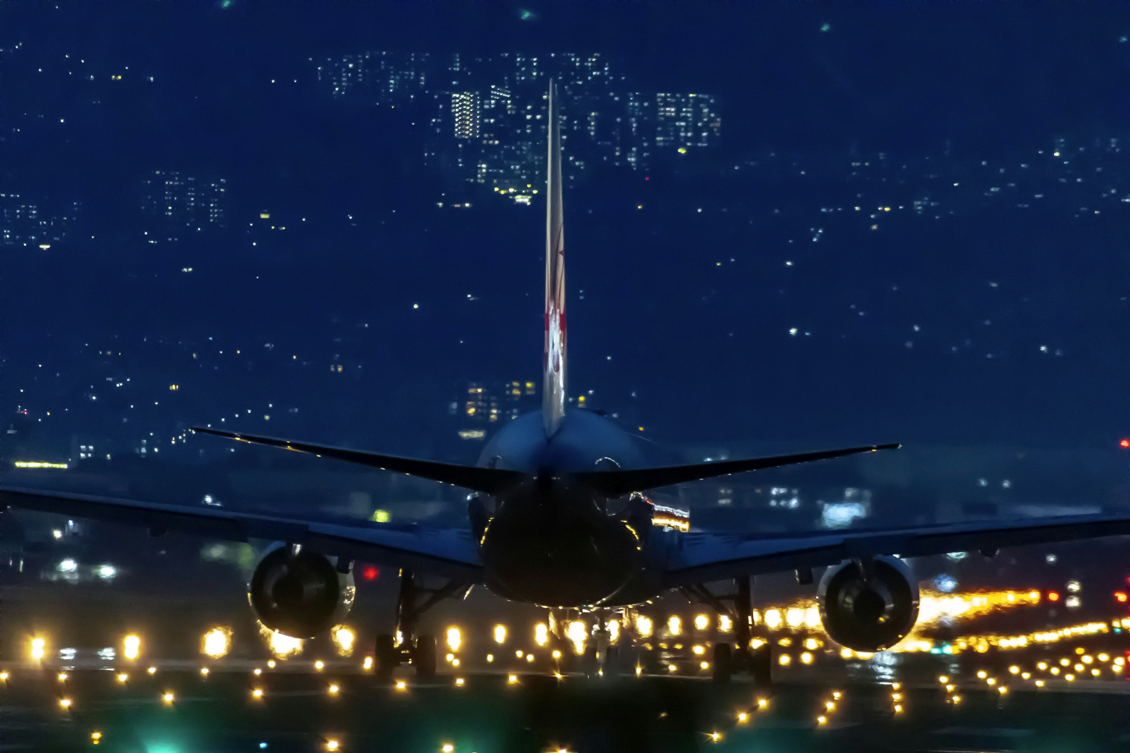 Rear view of an airplane landing at night with illuminated runway