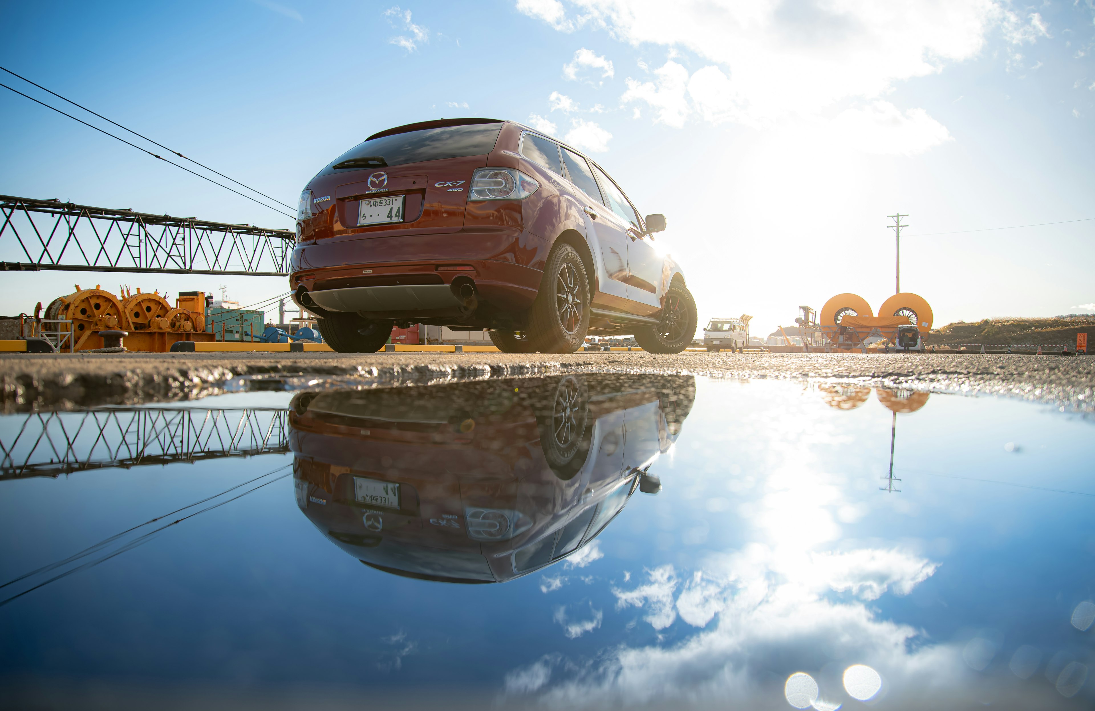 Red car reflected in a puddle with sunlight shining