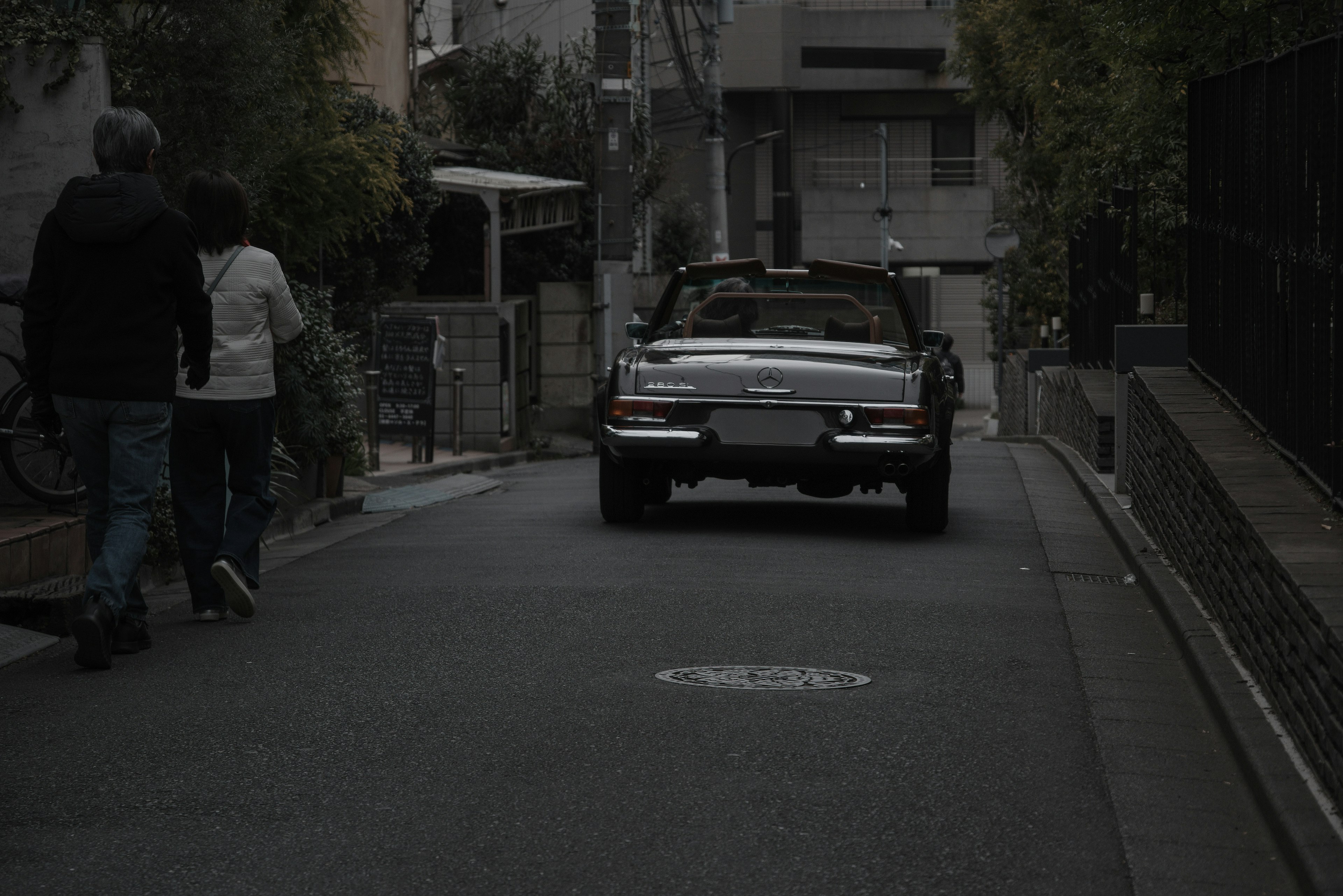 暗い通りを走る車と歩道を歩く人々のシーン