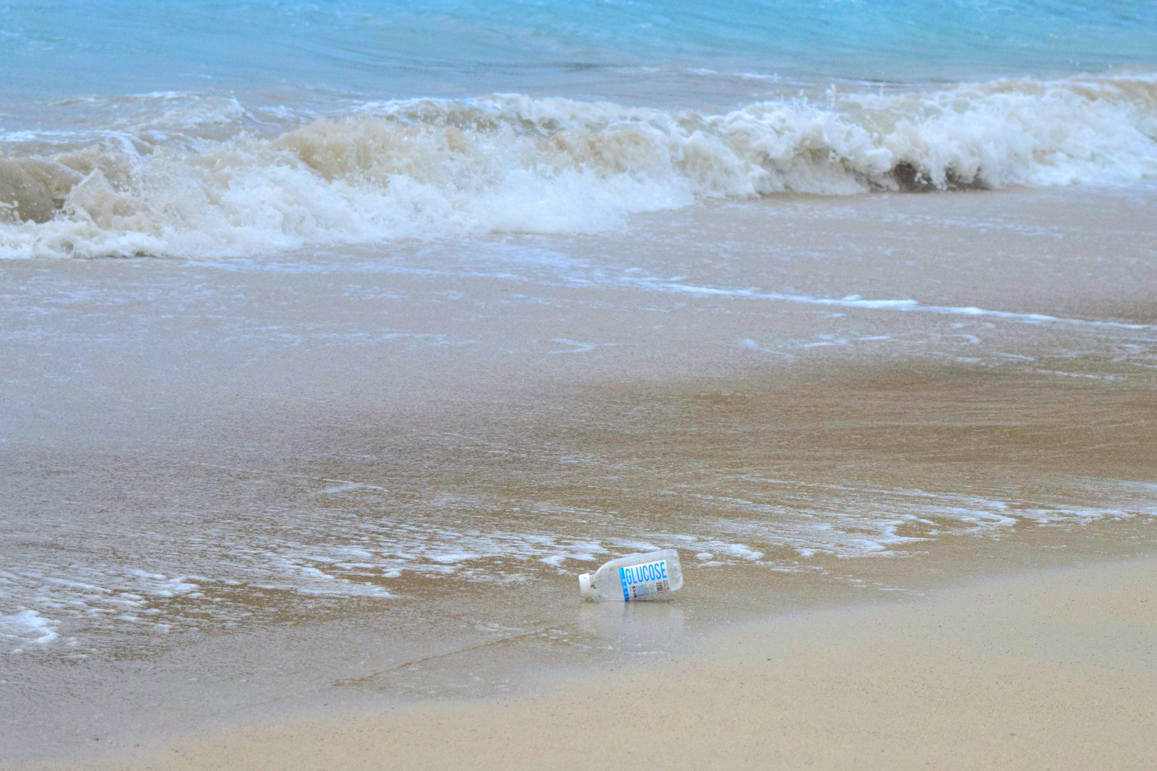 Una botella arrastrada en la playa con olas al fondo