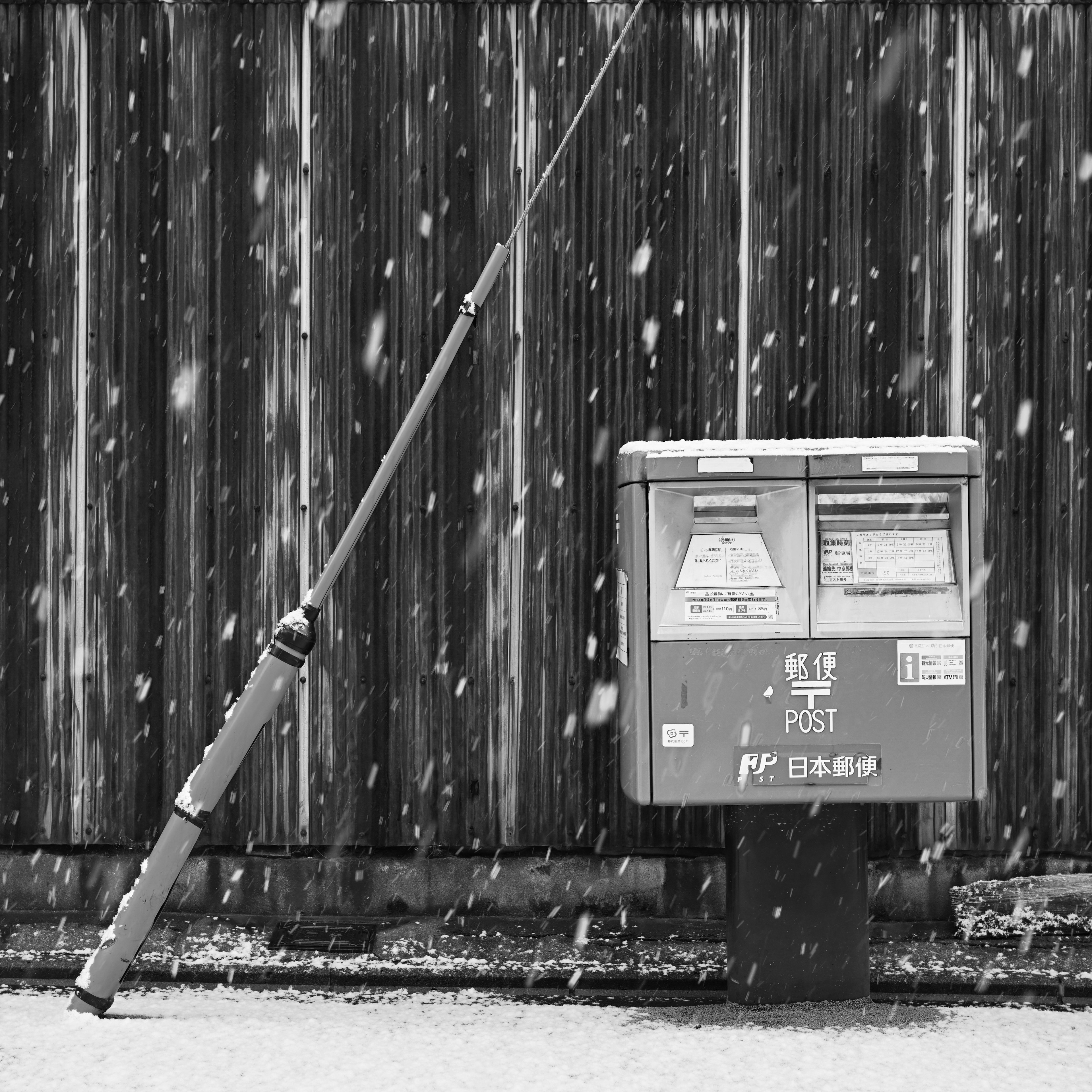 Red mailbox leaning against a wooden fence in the snow