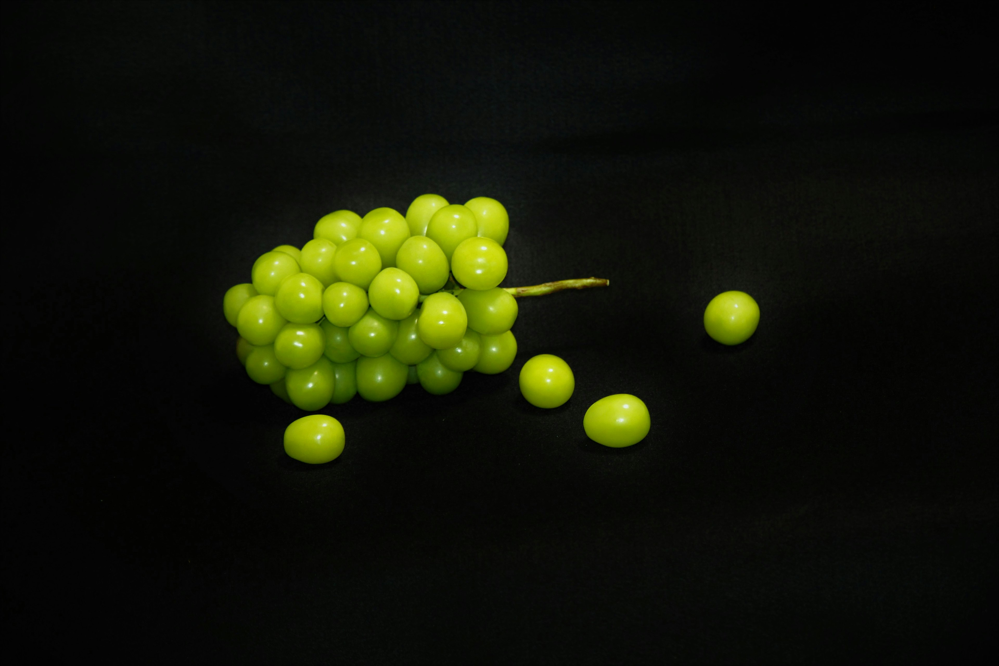 Une grappe de raisins verts avec quelques raisins éparpillés sur un fond noir