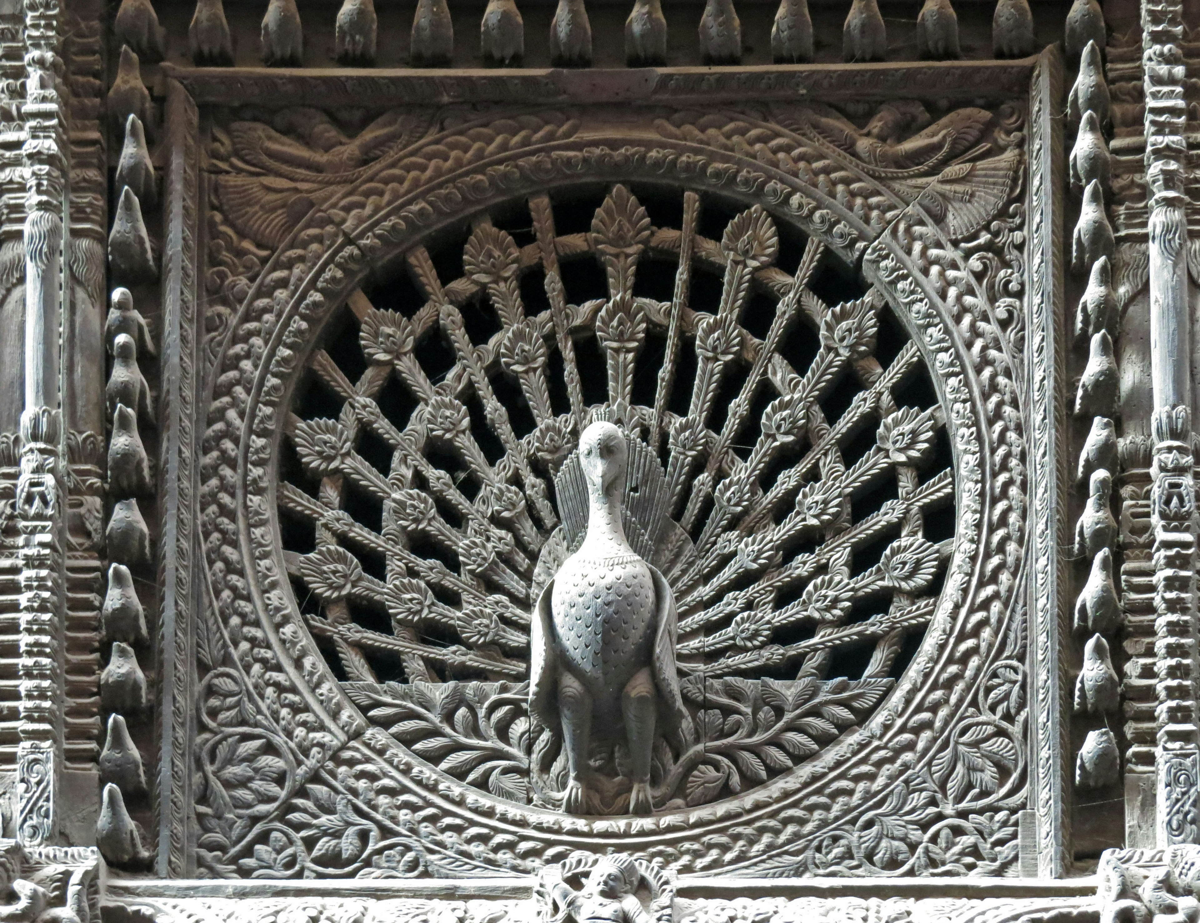 Decorative artwork featuring a peacock within intricate carvings