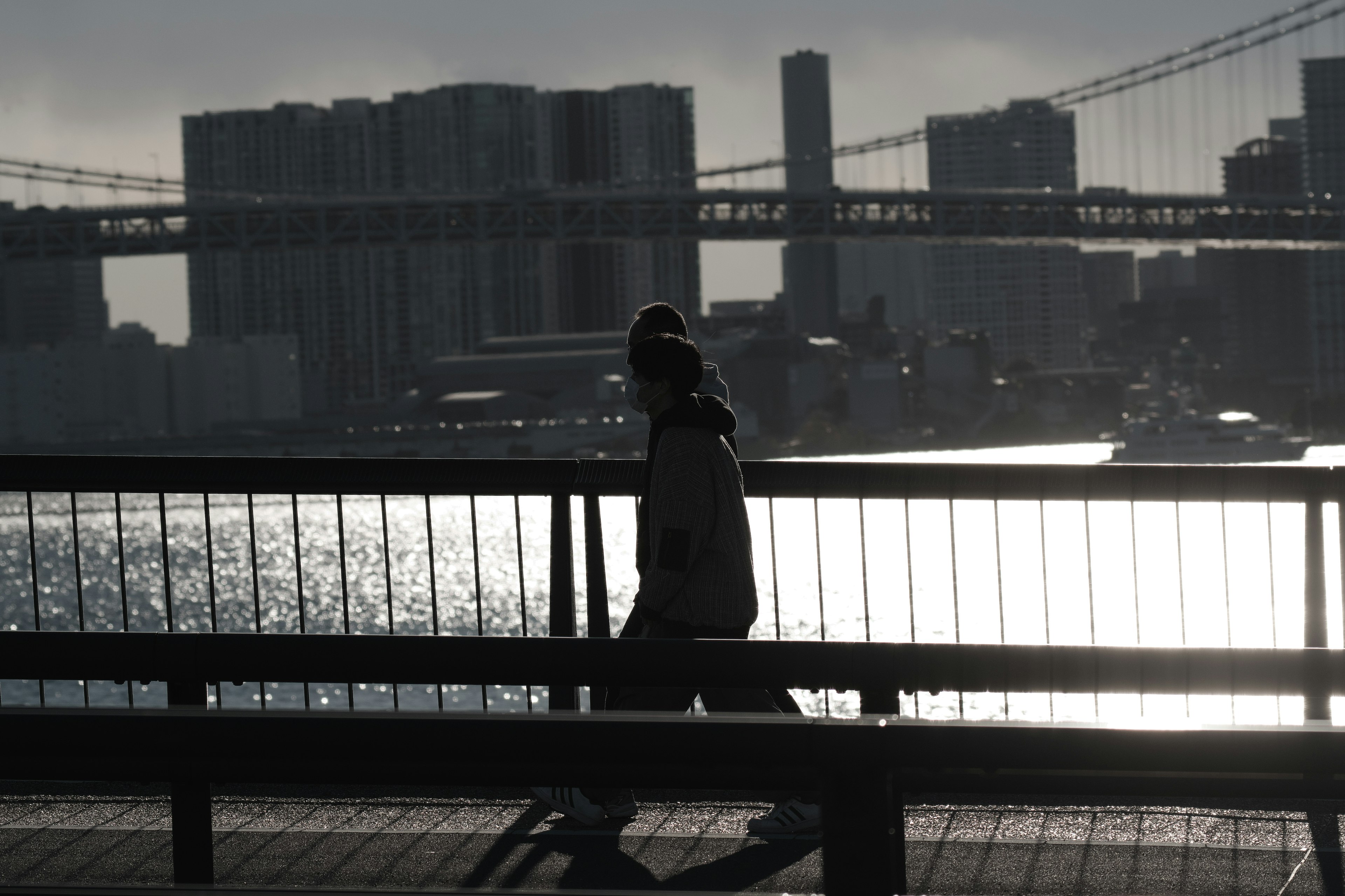 Silhouette of a person walking by the seaside at dusk with a bridge in the background