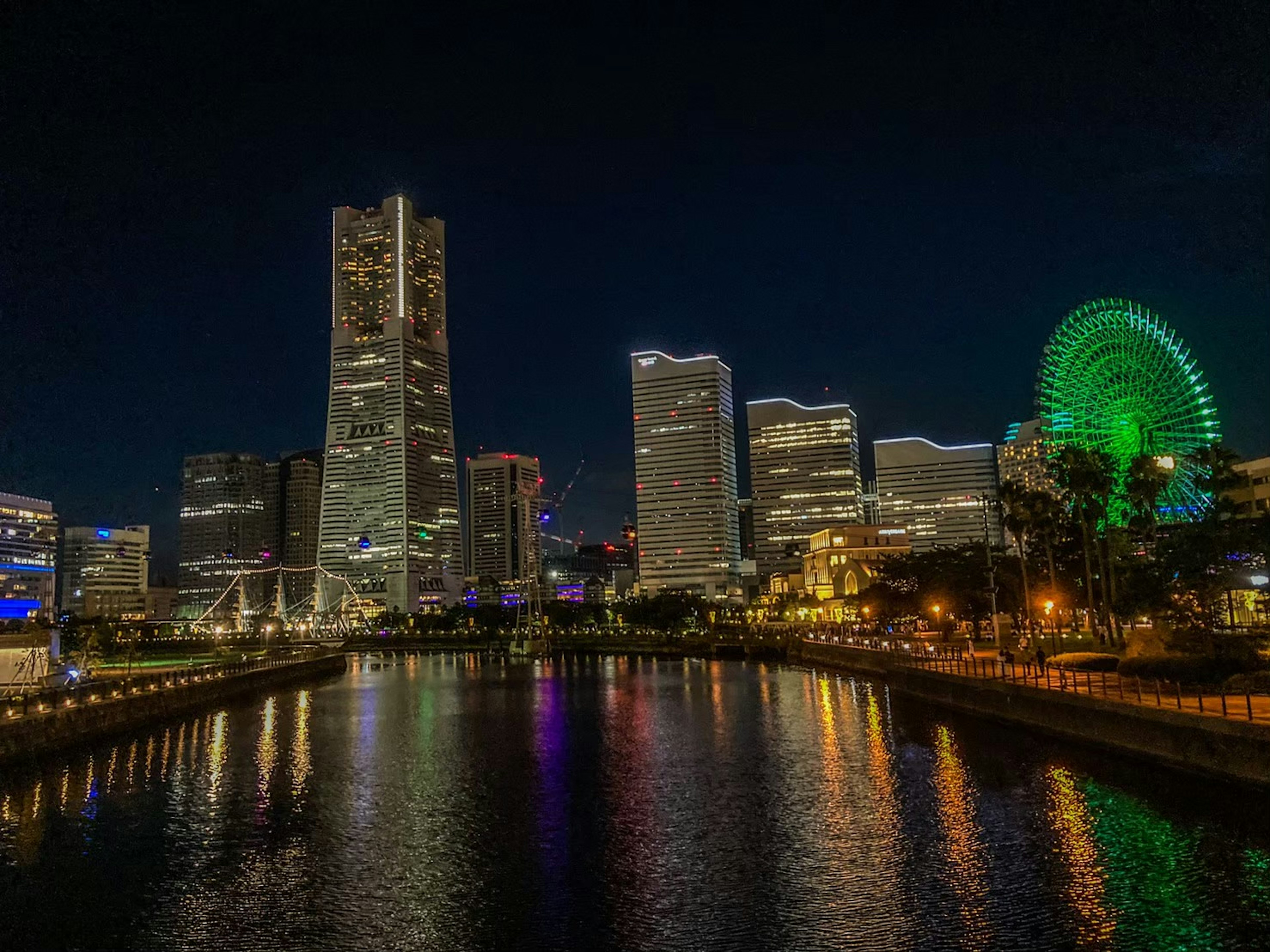 Vista nocturna de Yokohama con rascacielos iluminados y una noria reflejándose en el agua