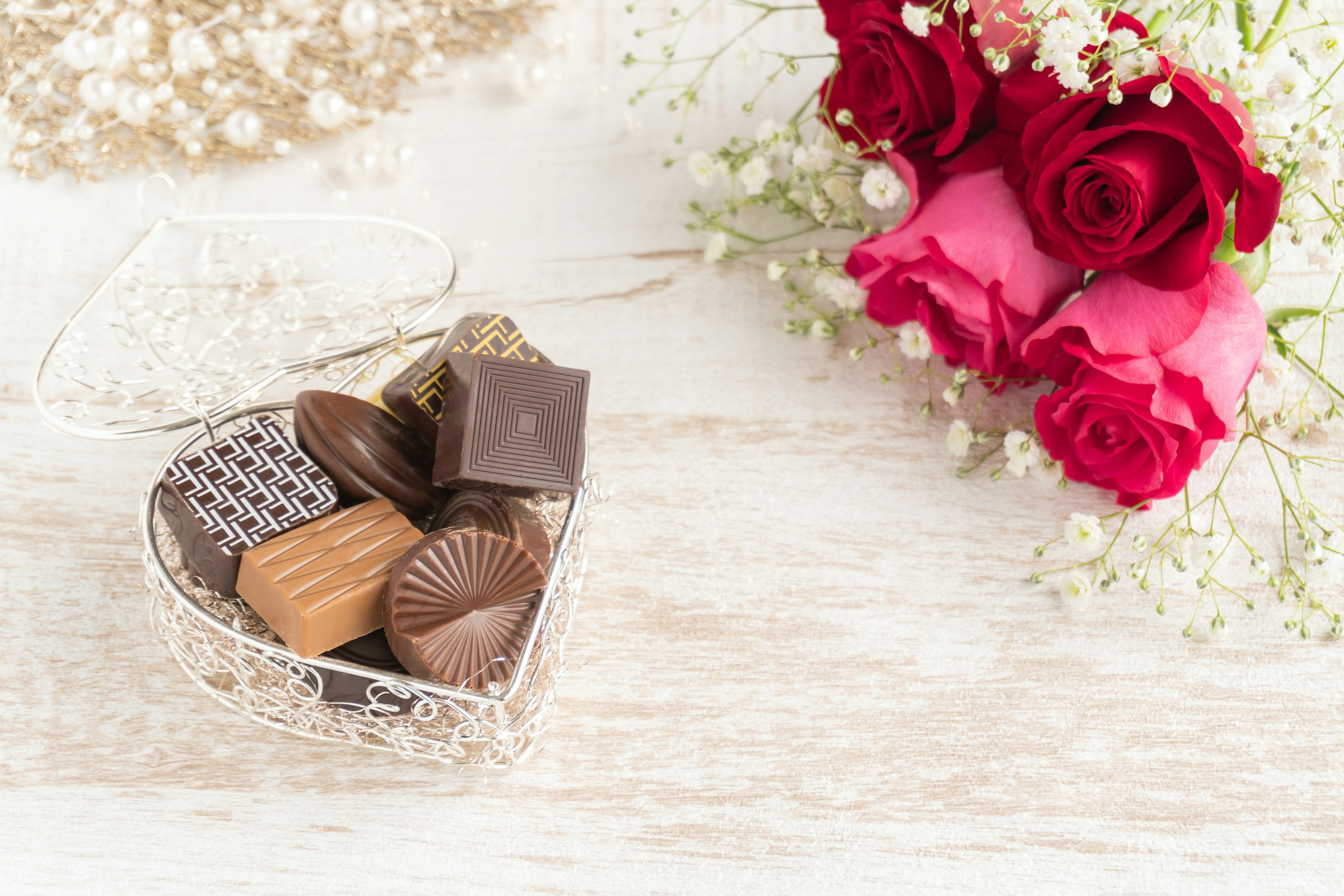 Cesta en forma de corazón llena de chocolates y un ramo de rosas rojas