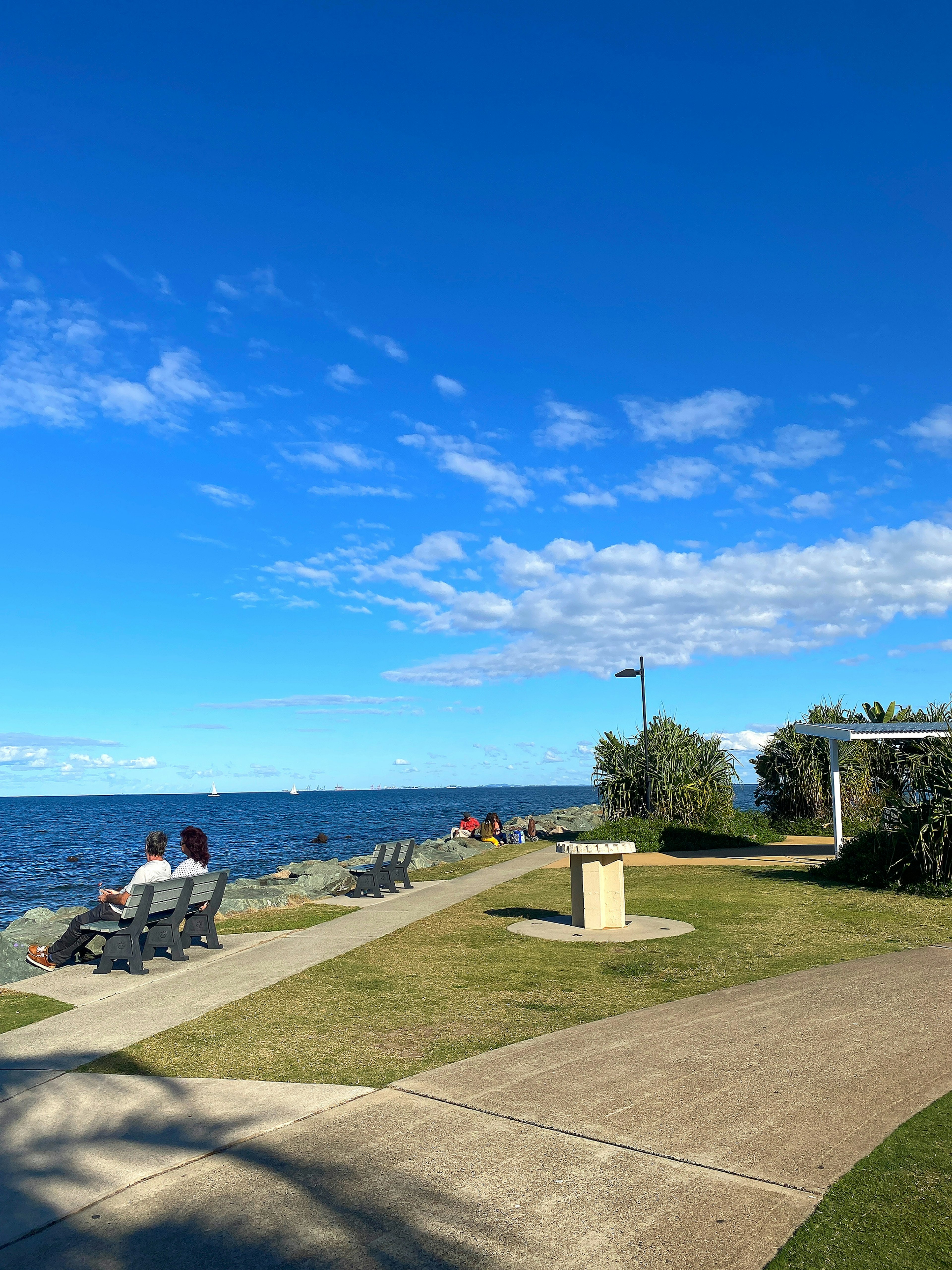 Paar sitzt am Meer unter einem blauen Himmel mit einem Parkweg