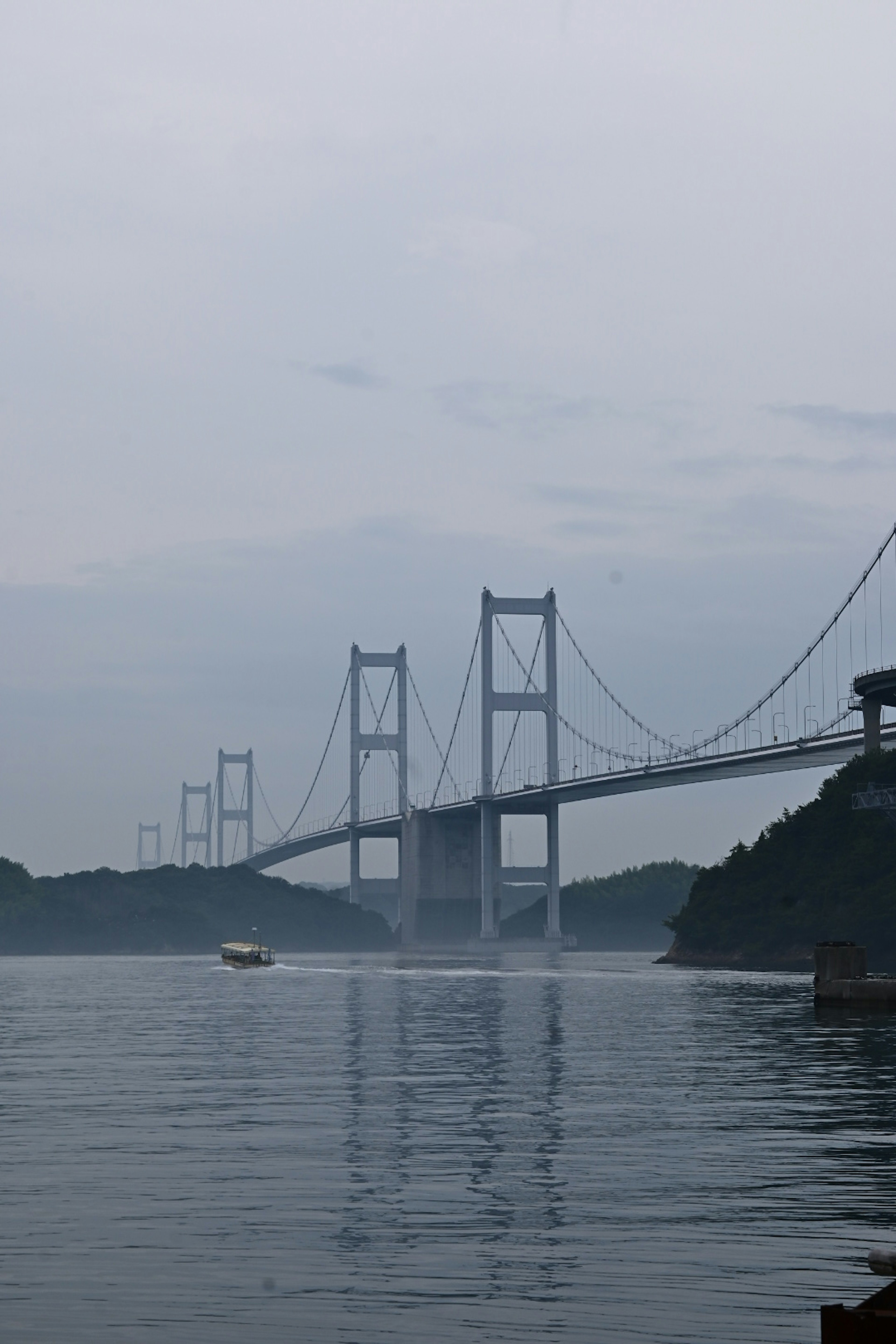 Bridge emerging through fog with calm water surface