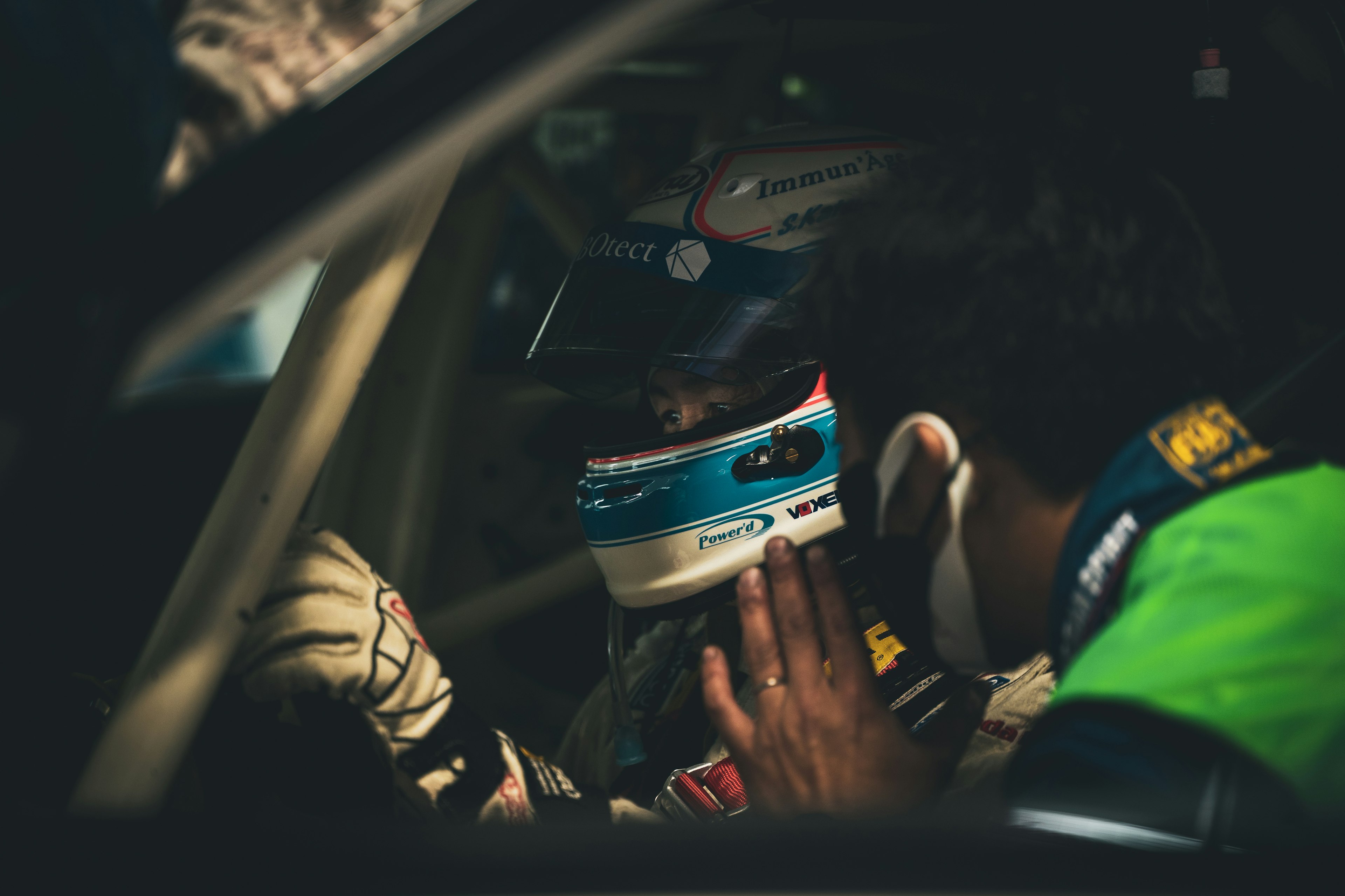 Driver in a racing car wearing a helmet with a support staff member assisting