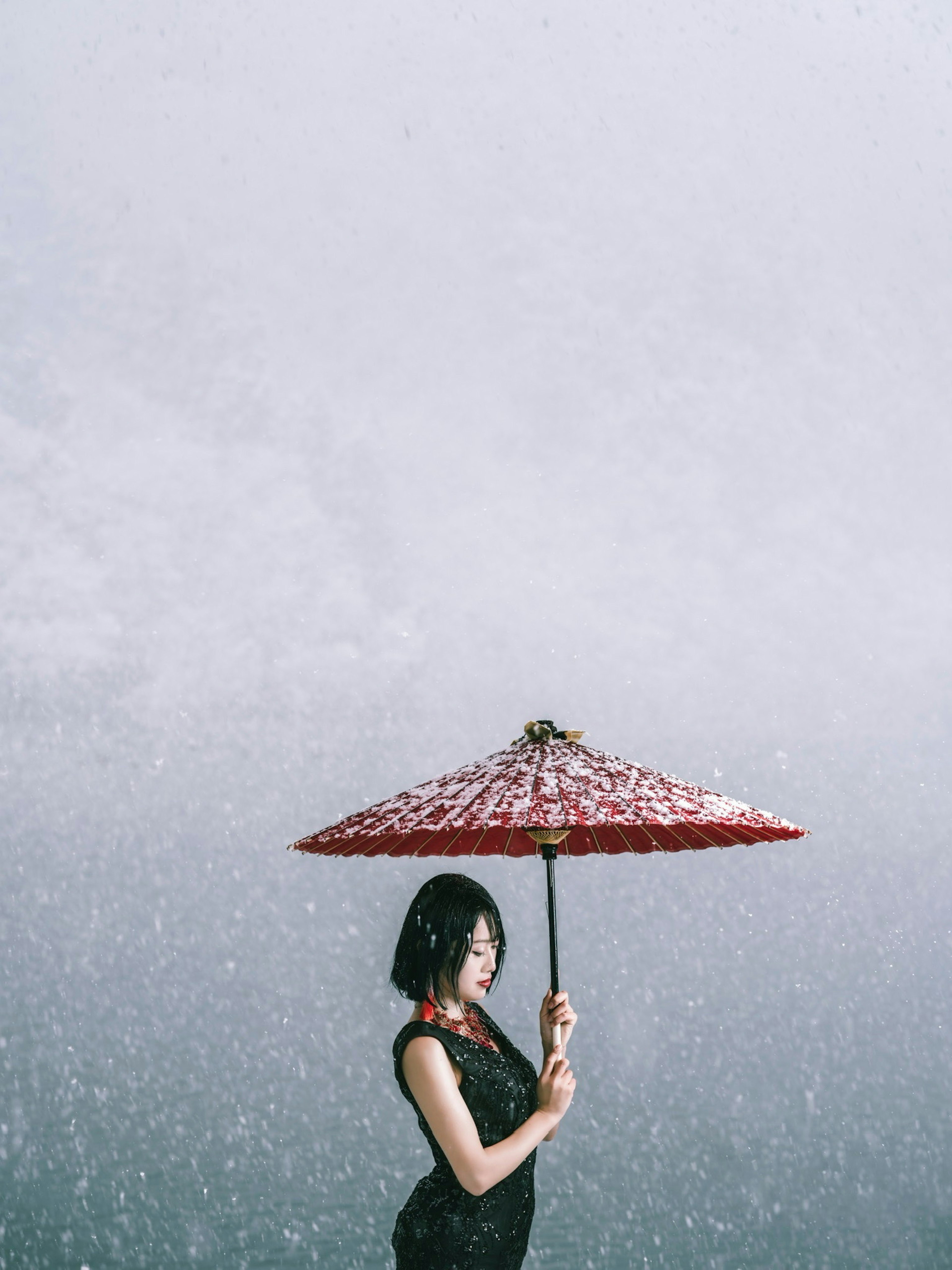 Woman in black dress holding red umbrella in a rainy scene