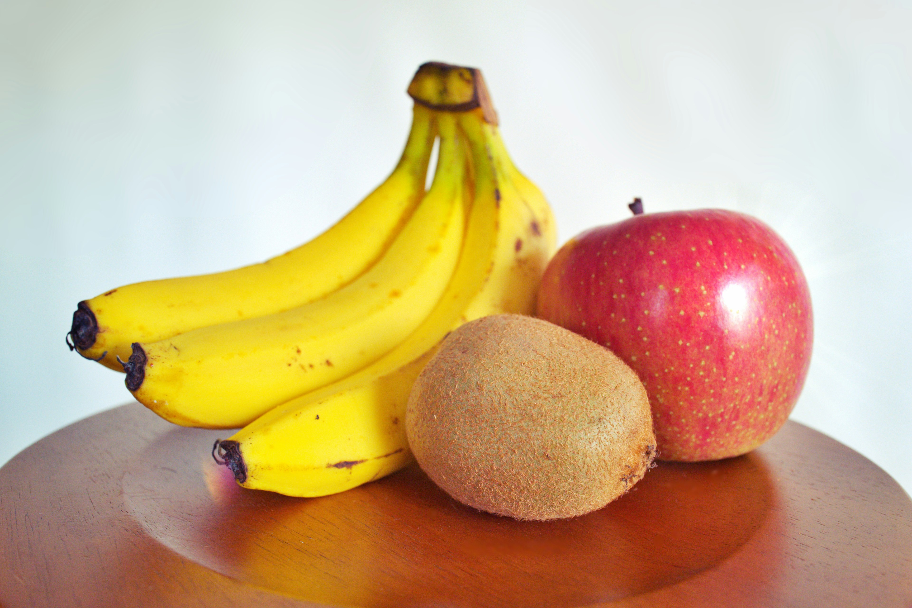 A bunch of bananas an apple and a kiwi on a wooden table