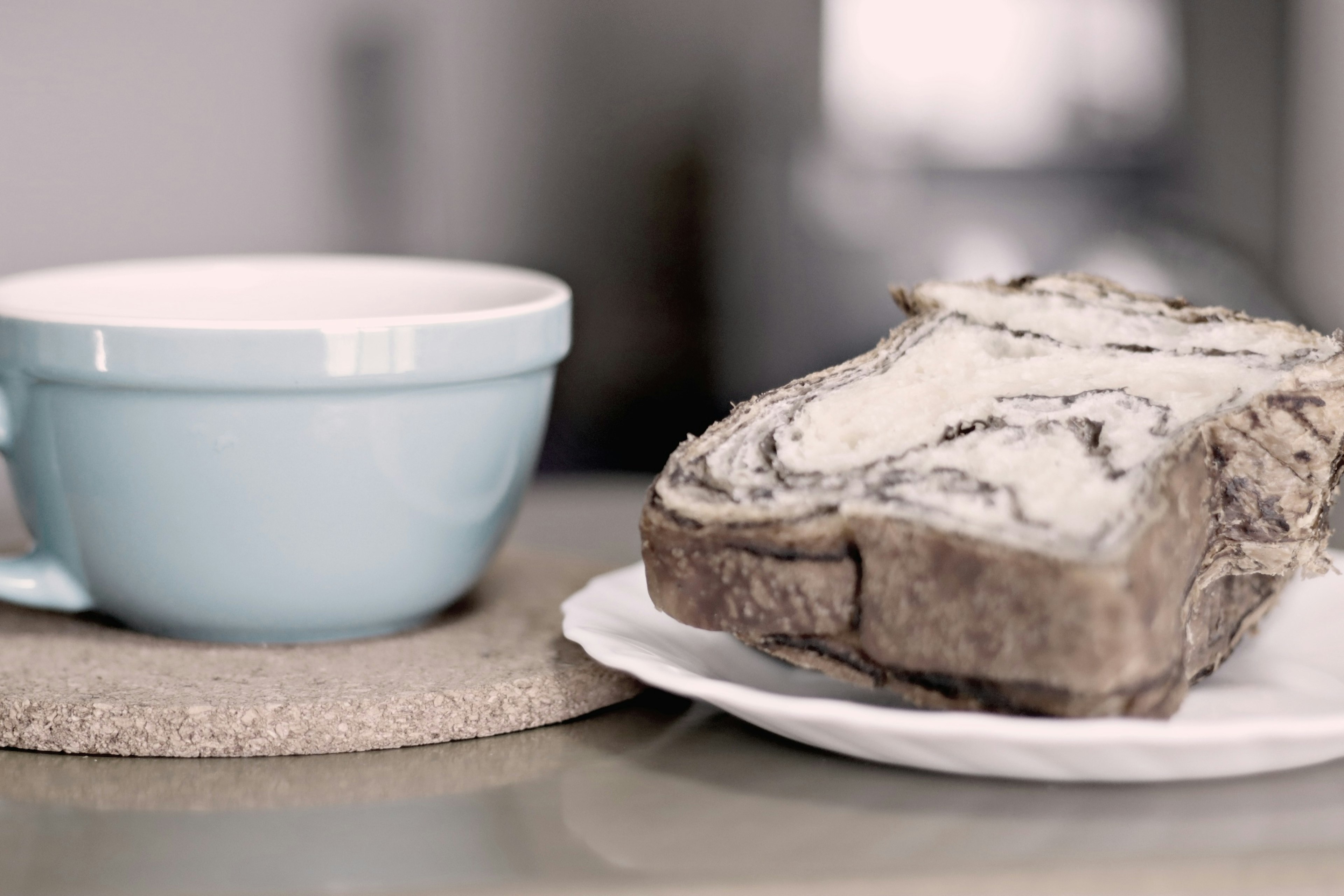 A light blue cup with a drink beside a slice of patterned bread on a plate