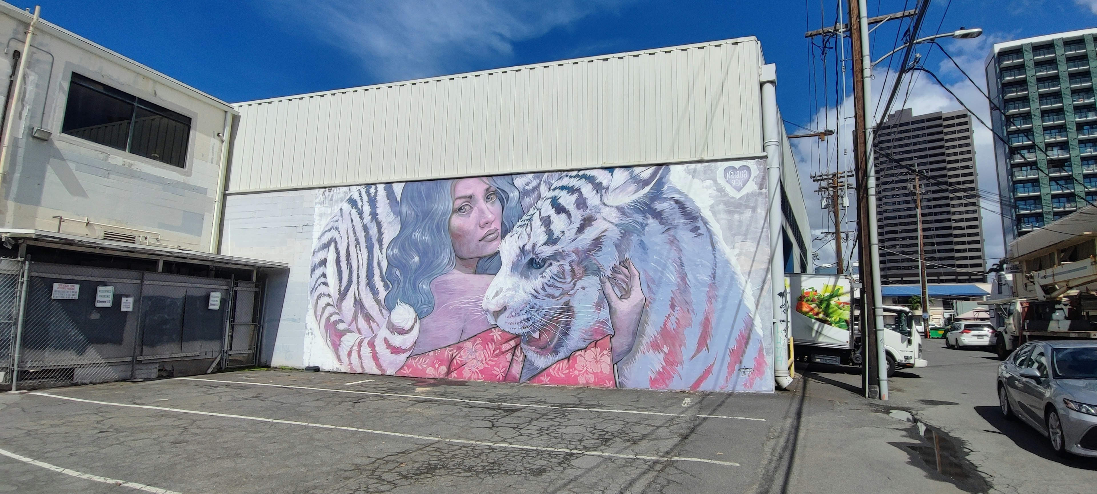 Gran mural de un tigre y una mujer en una pared blanca en un entorno urbano