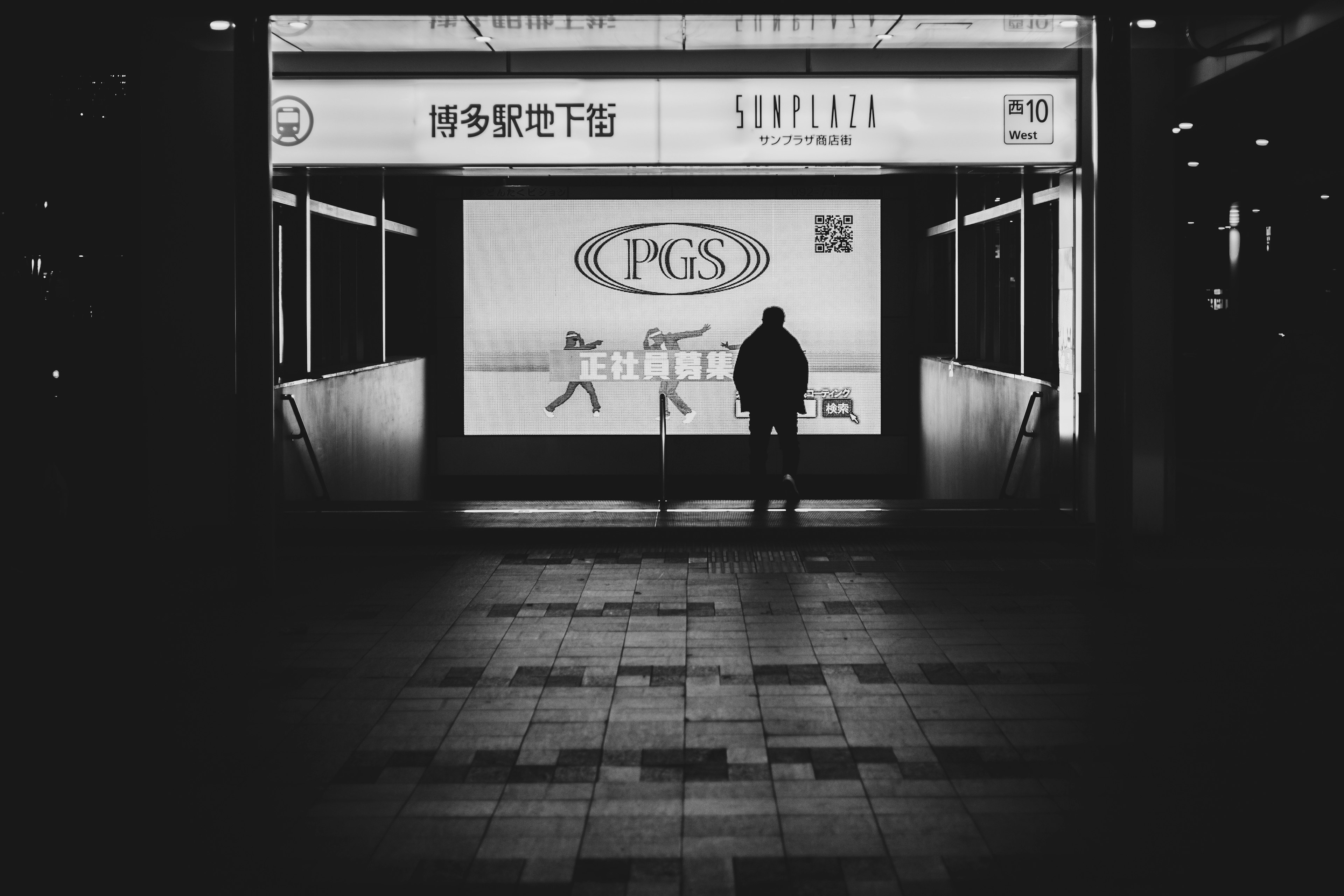 A person standing in a dimly lit area with a bright advertisement