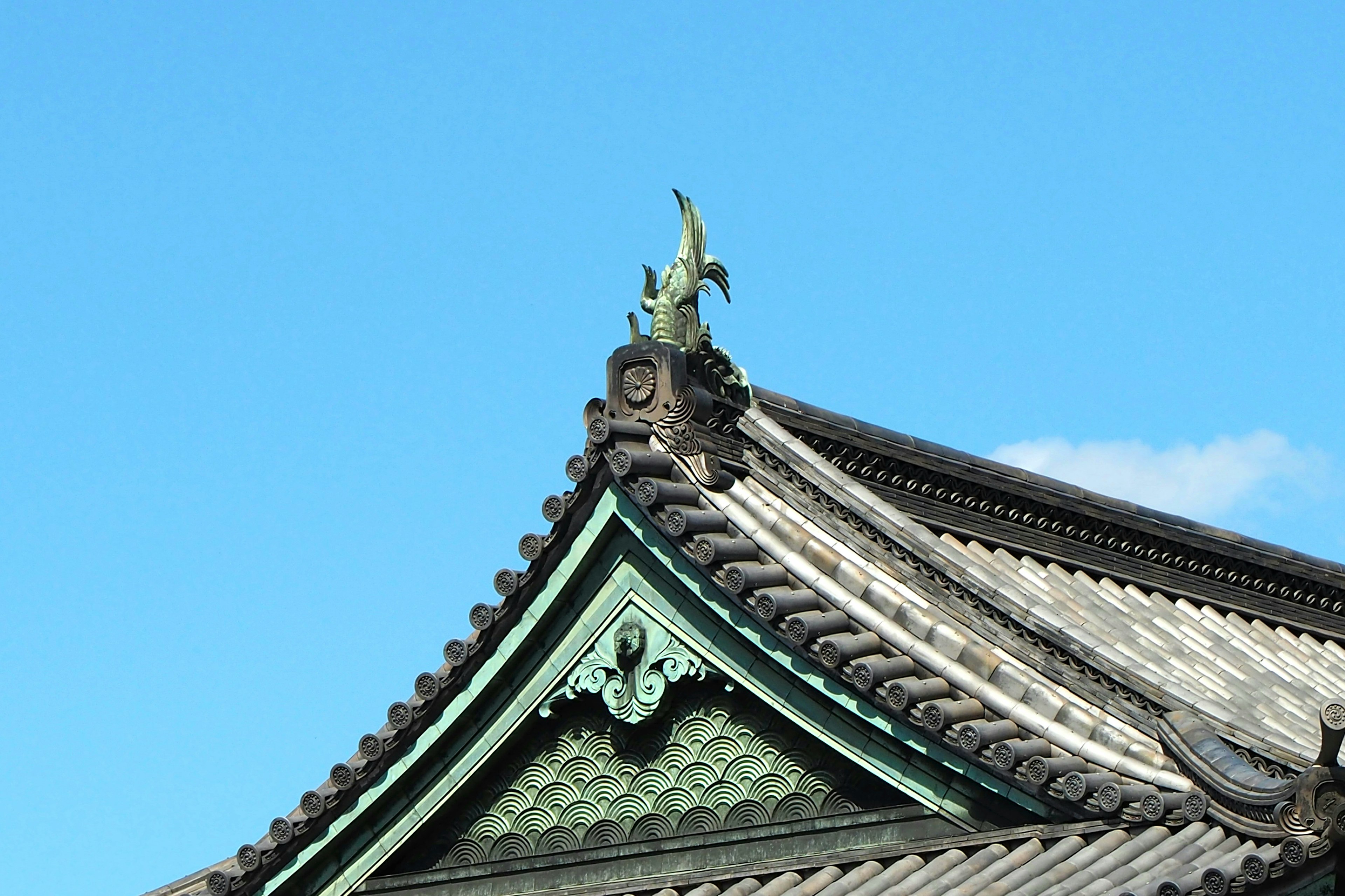 Parte de un techo japonés tradicional bajo un cielo azul con tejas y tallas decorativas