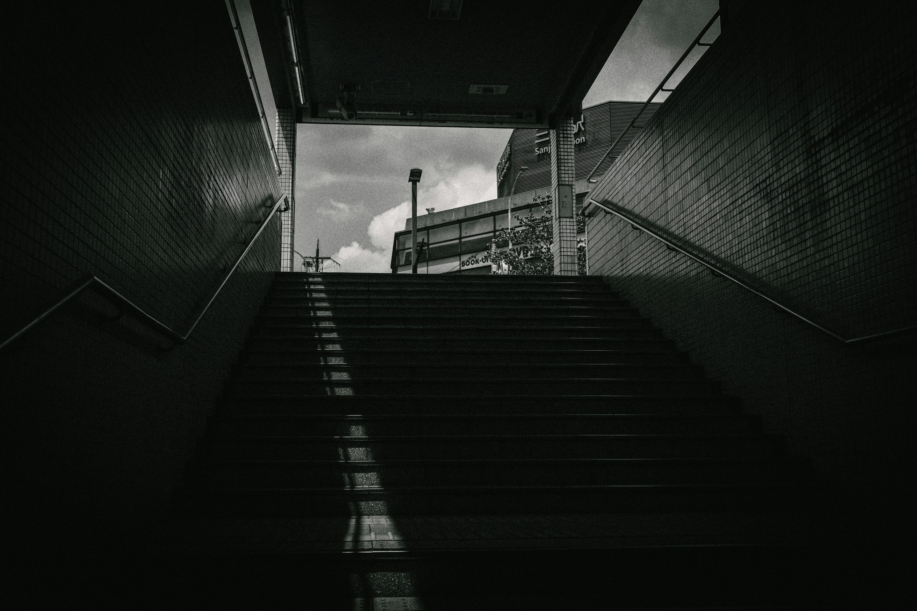 Blick von unten auf eine Treppe, die zu einem dunklen Tunnel mit Ausgang nach außen führt