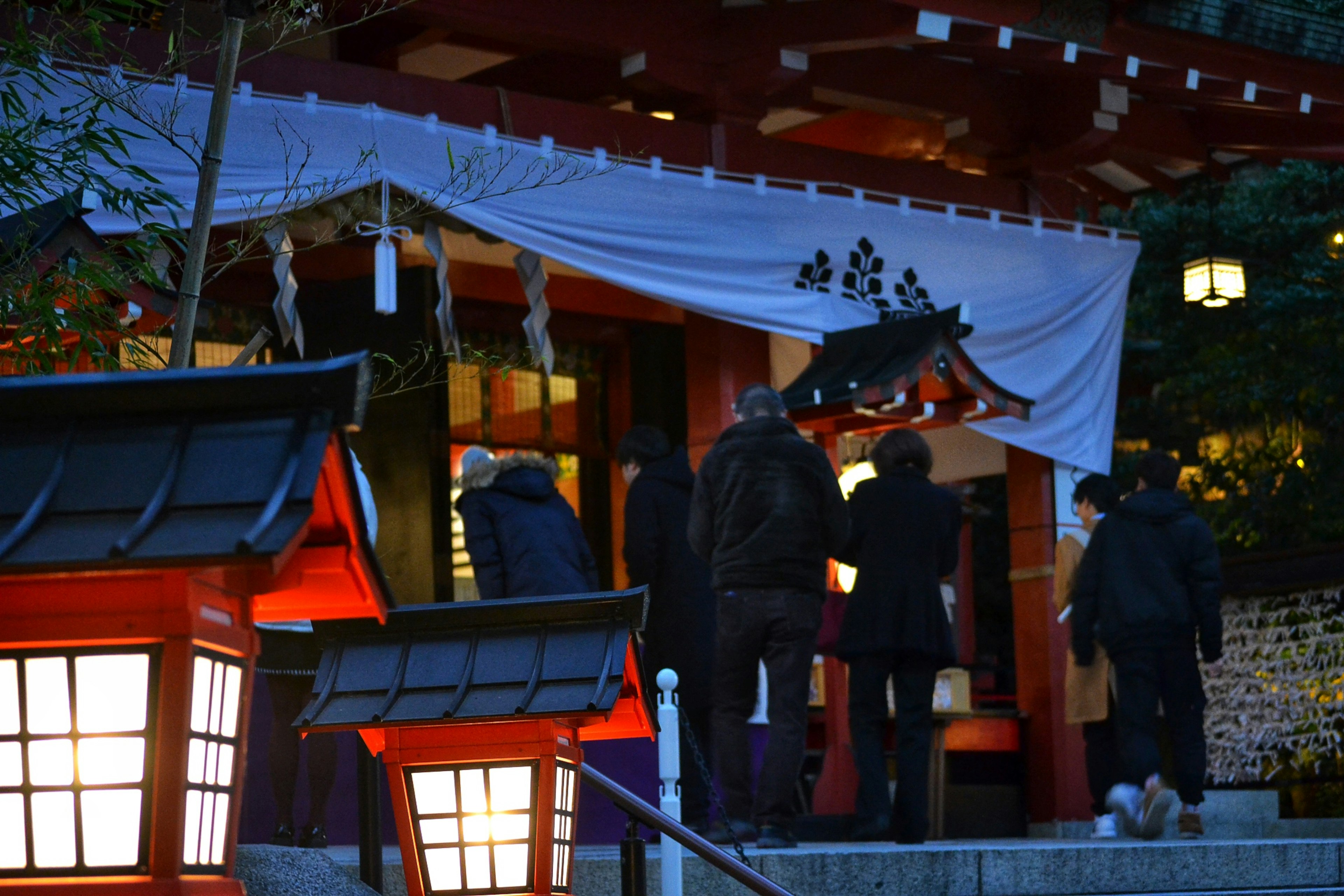 People approaching a shrine at night illuminated by red lanterns