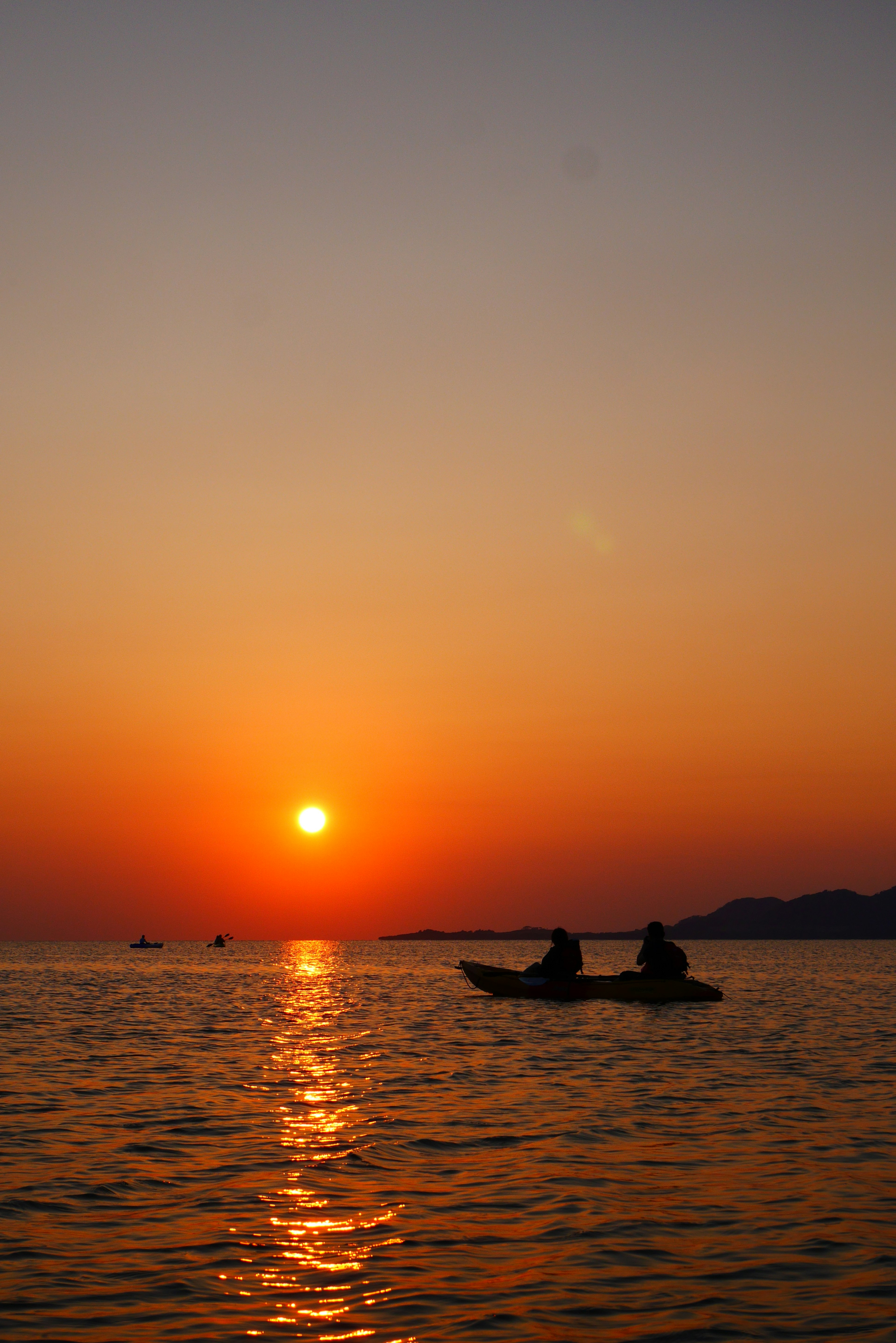 在平静的海面上，夕阳下两人划皮划艇的剪影